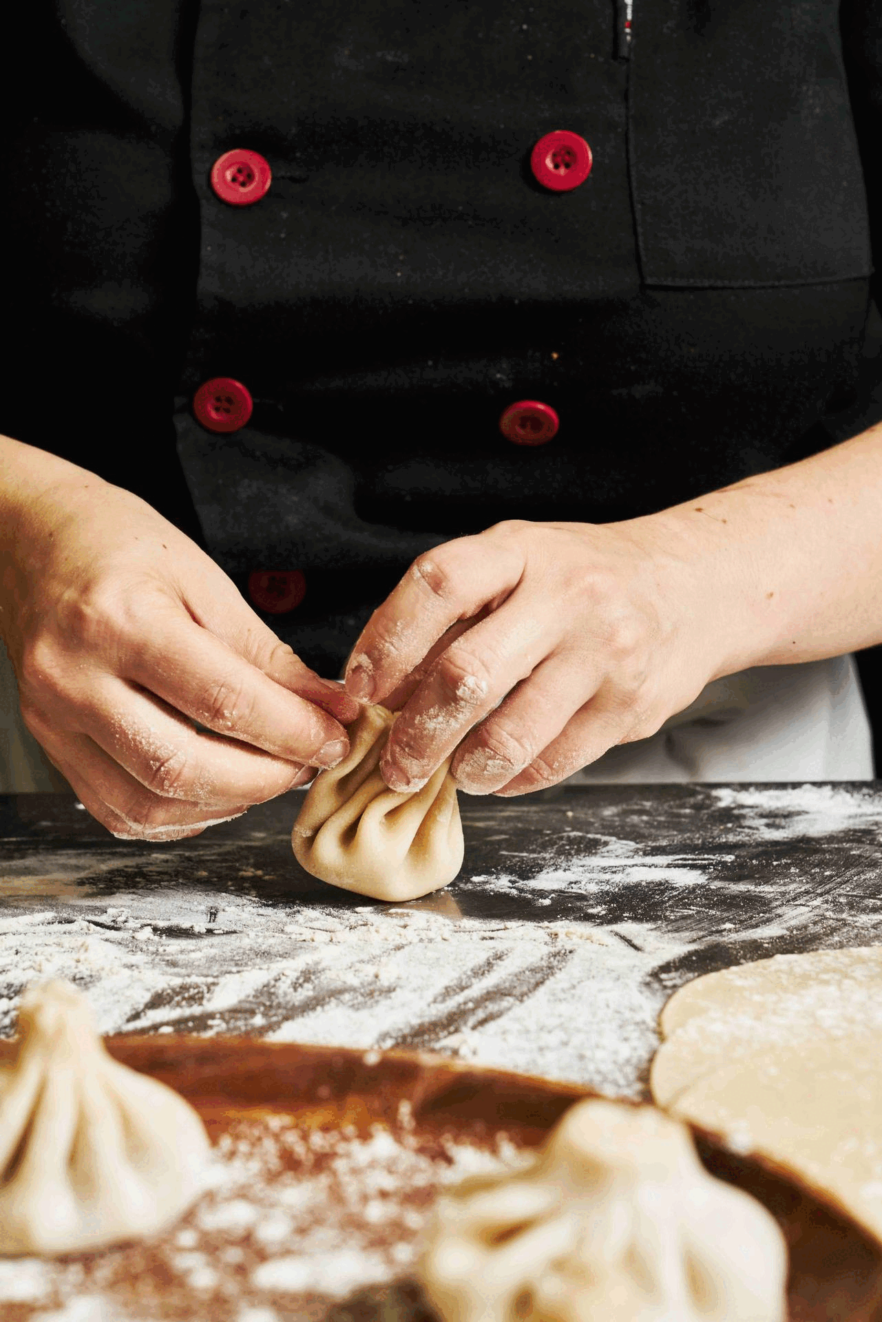 Hands pleating khinkali dumplings on a floured board