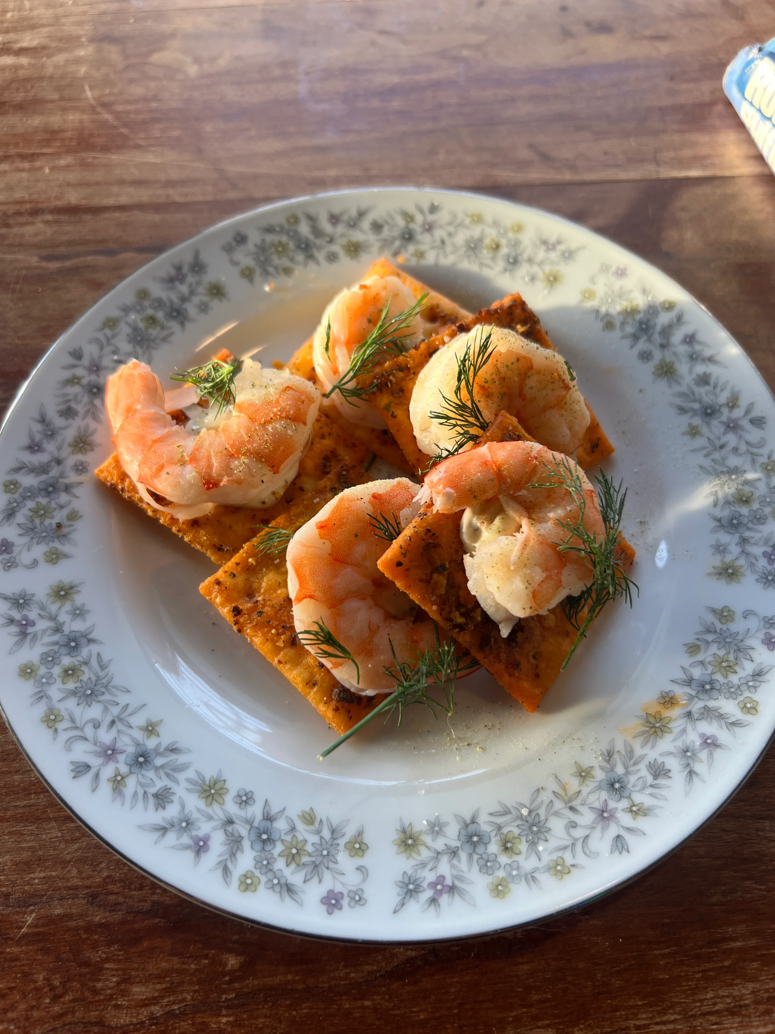 A decorative plate featuring shrimp on seasoned crackers, garnished with fresh dill. The arrangement showcases the shrimp and crunchy texture of the crackers.