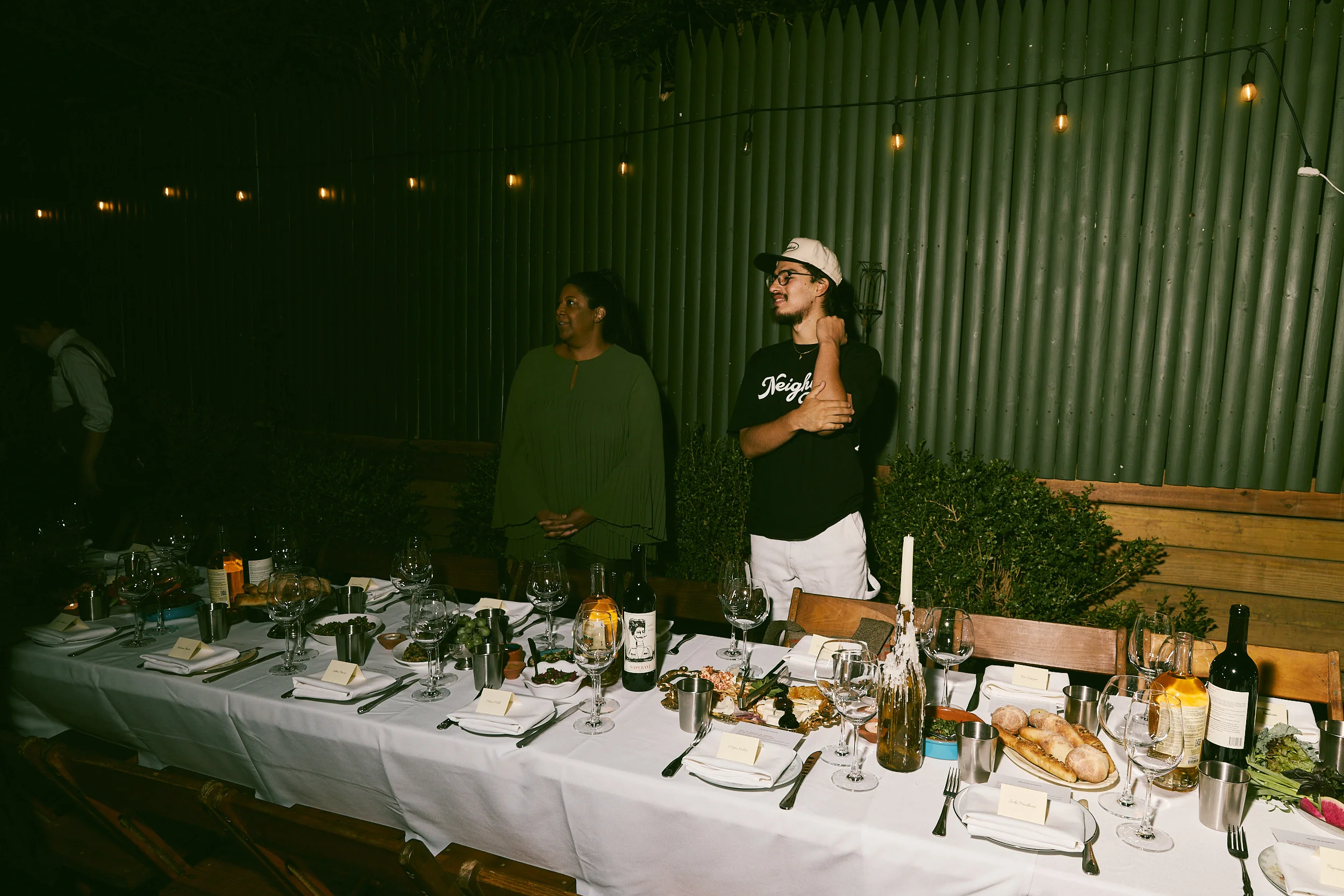 Elegant outdoor restaurant dinner with string lights, wine, and communal dining table