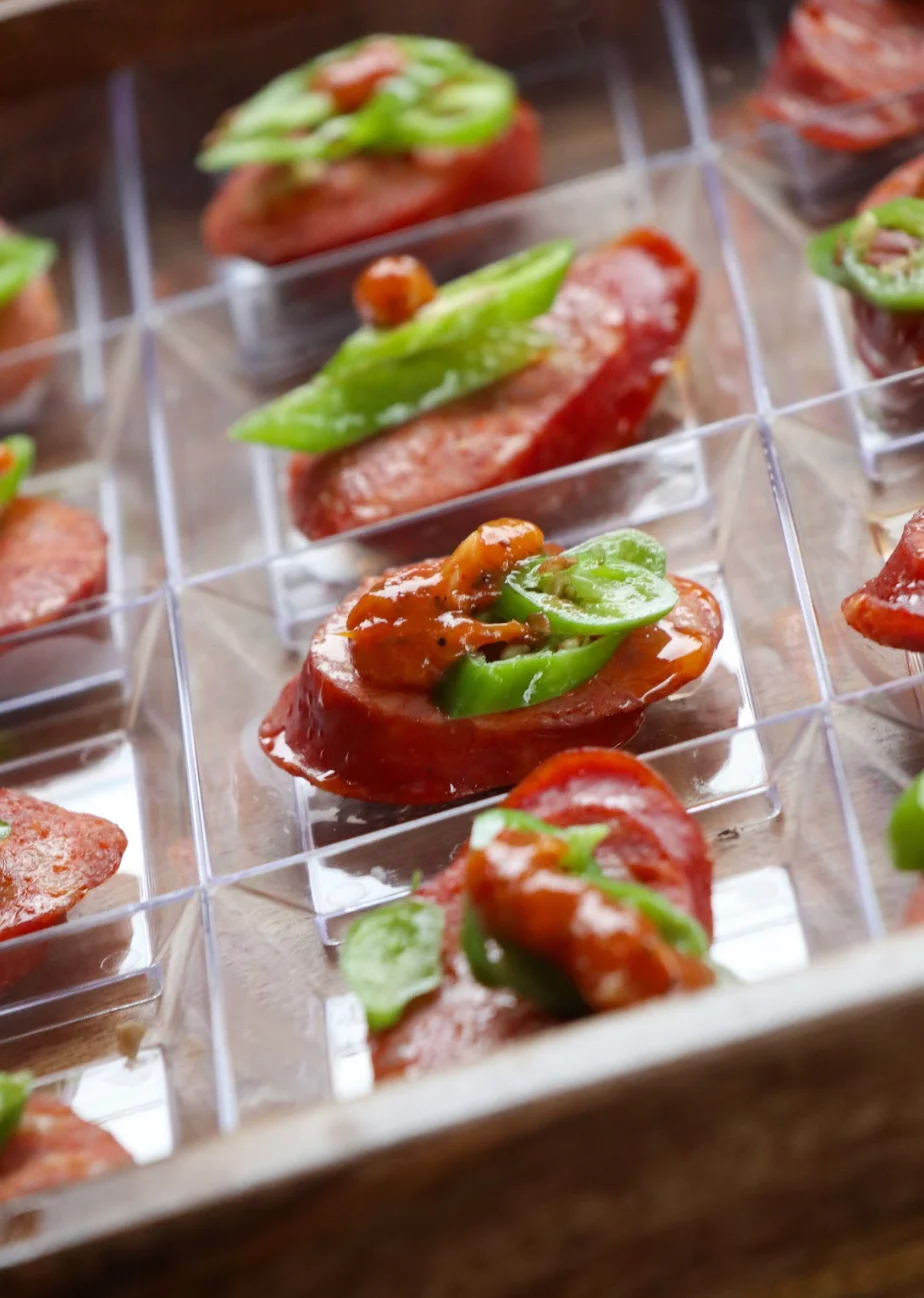 Sliced sausage topped with green peppers in clear serving cups.