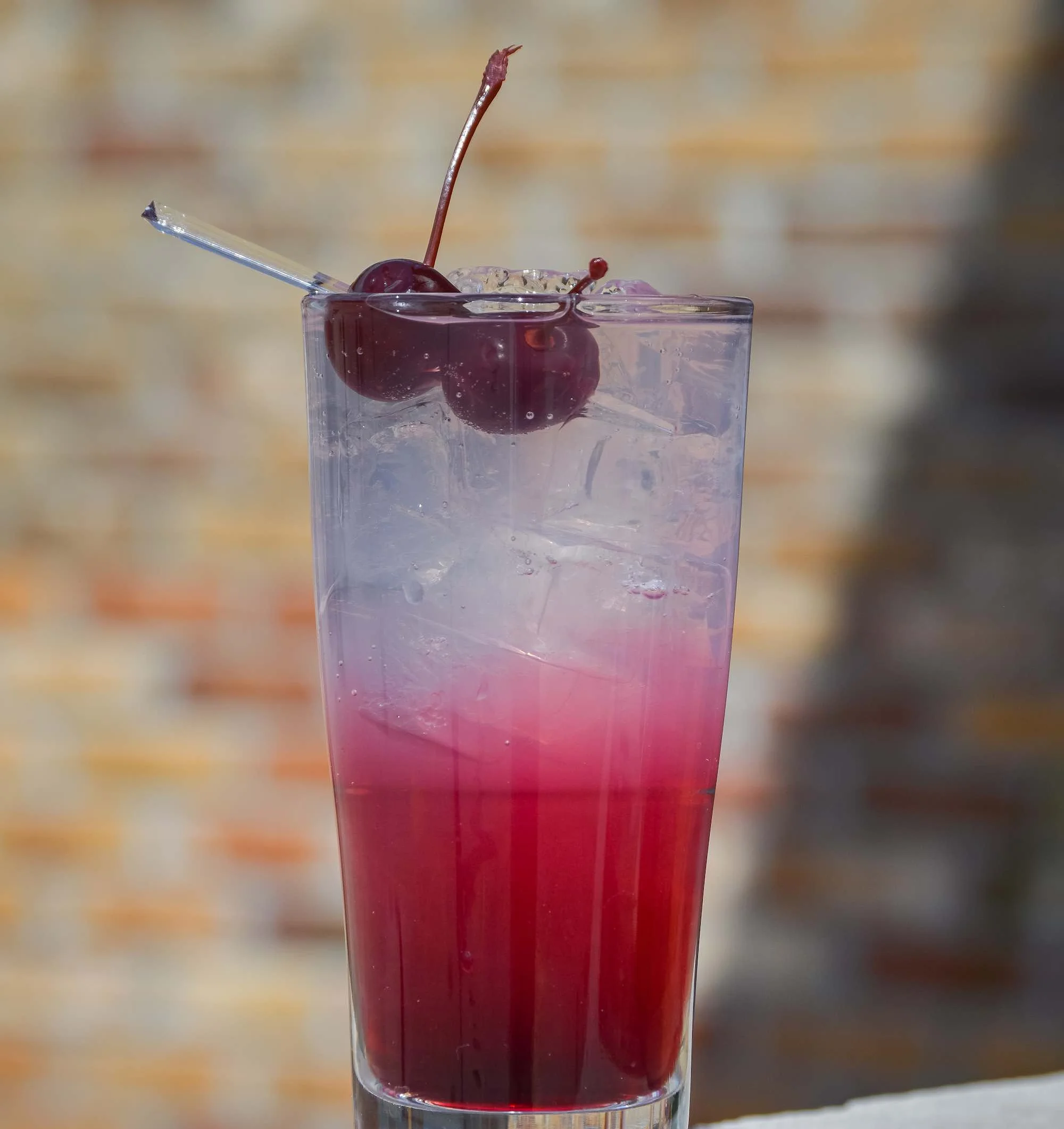 Glen Collins cocktail in beautiful shades of pink and purple in front of a brick wall