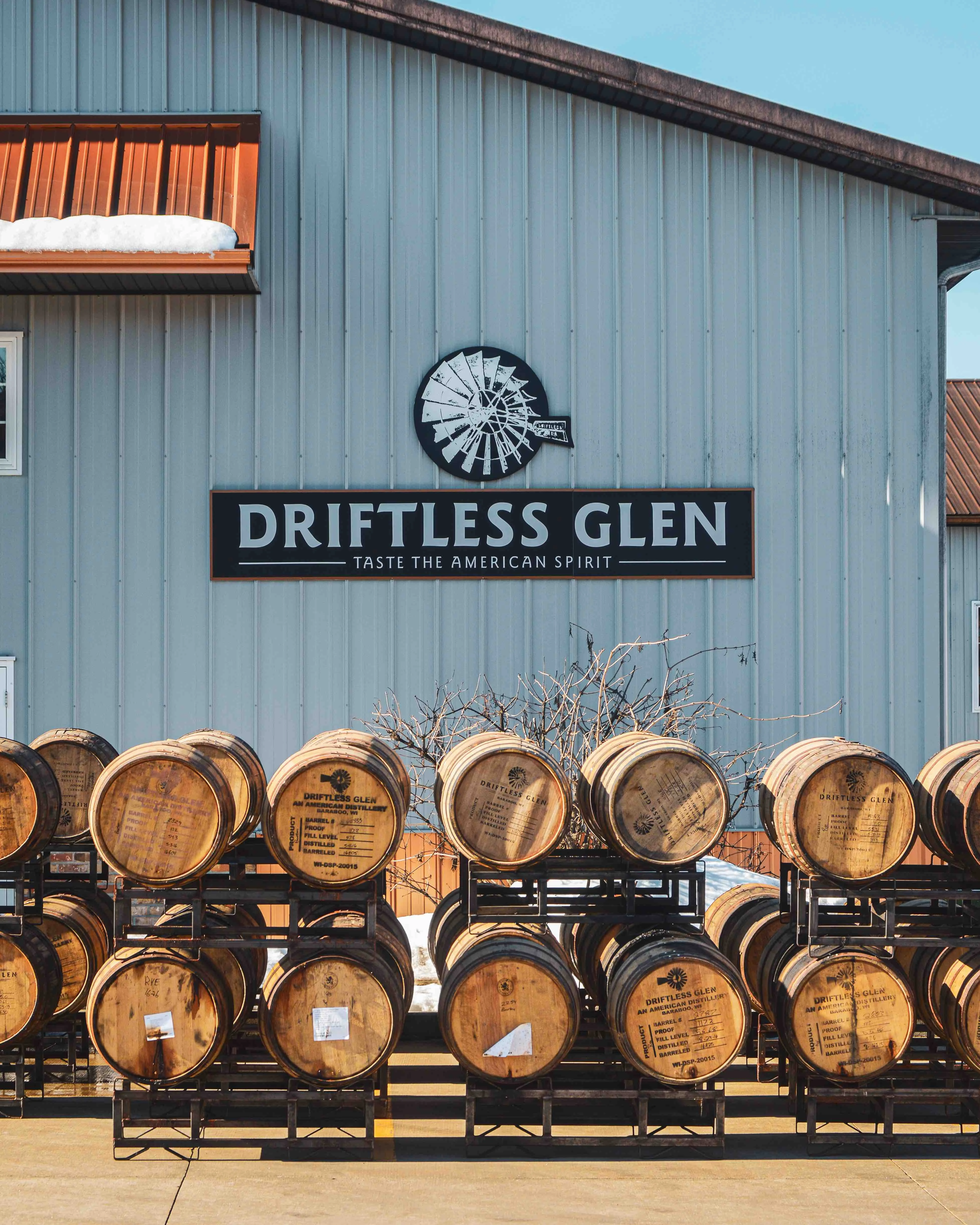 A few rows of barrels sit outside in front of the building with a little bit of snow hanging around on the eaves