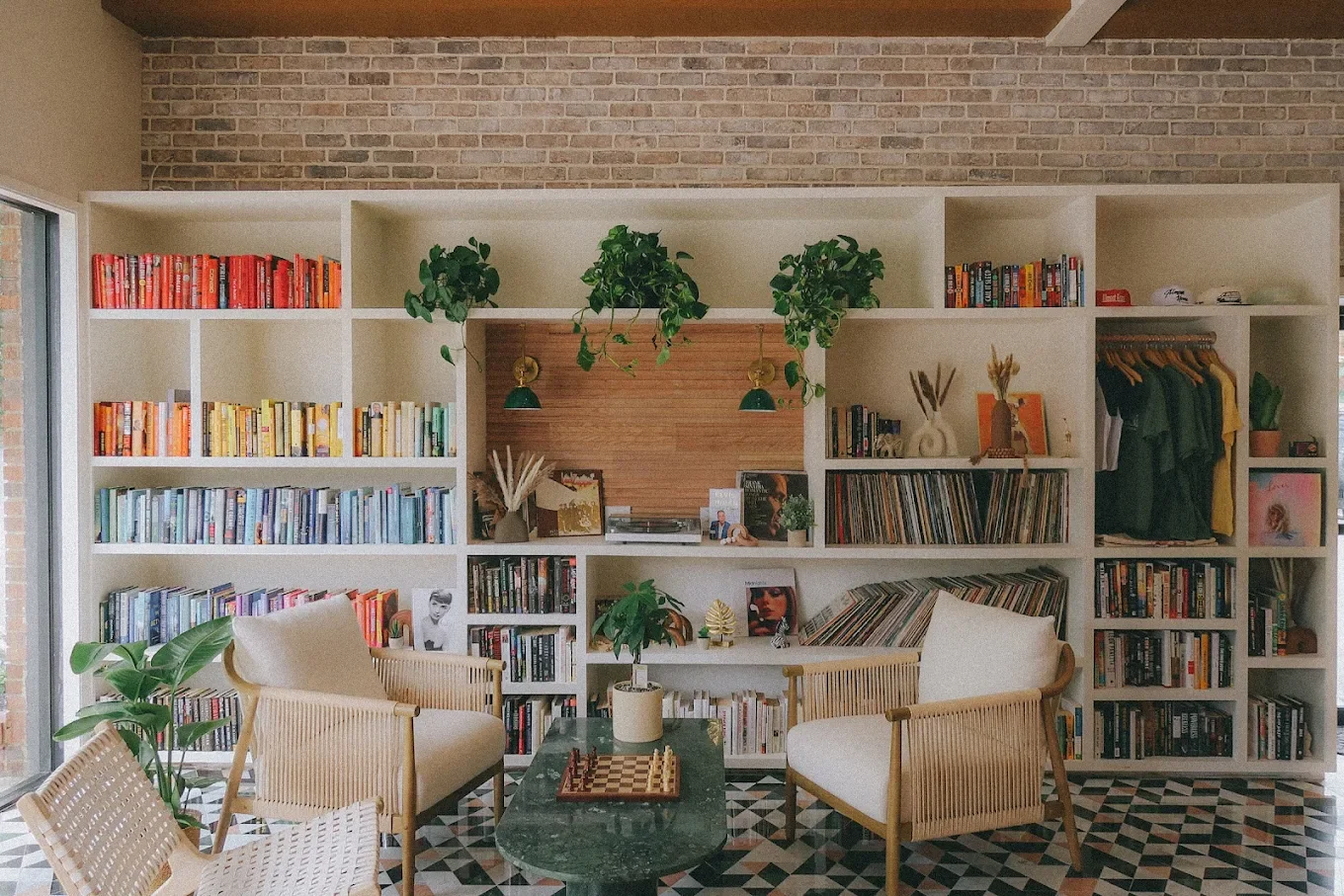 A cozy reading nook featuring a white bookshelf filled with books in various colors and genres. Two stylish chairs are positioned in front, alongside a small coffee table on a patterned floor.