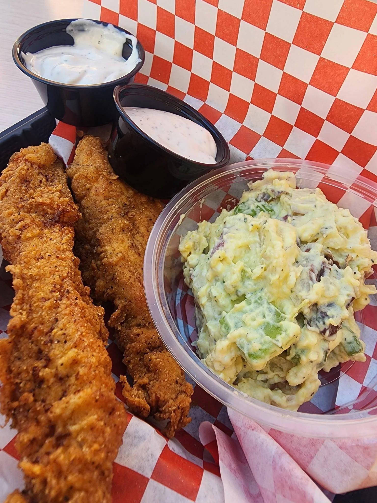 Fried fish tenders served with a side of creamy potato salad and two dipping sauces.