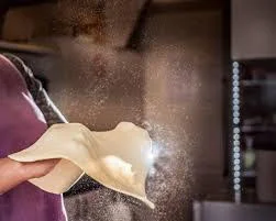 A person tossing pizza dough in the air with flour particles floating around.