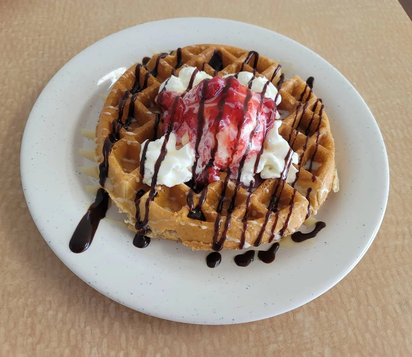 Belgian waffle topped with whipped cream and strawberry sauce