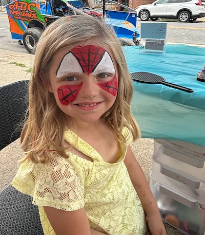 Child with Spider-Man face paint smiling at a table