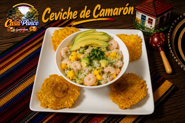A bowl of shrimp ceviche garnished with avocado, served with crispy fried plantains on a white plate.