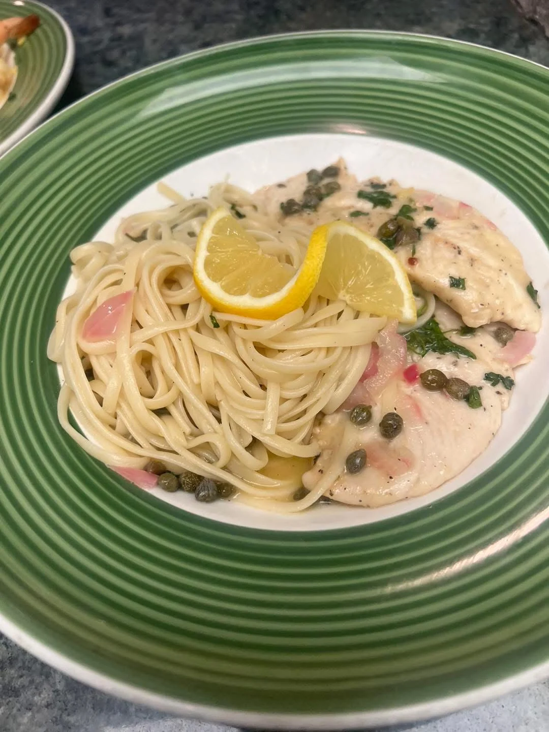 A plate of lemon-flavored chicken served with spaghetti and capers, garnished with lemon slices.