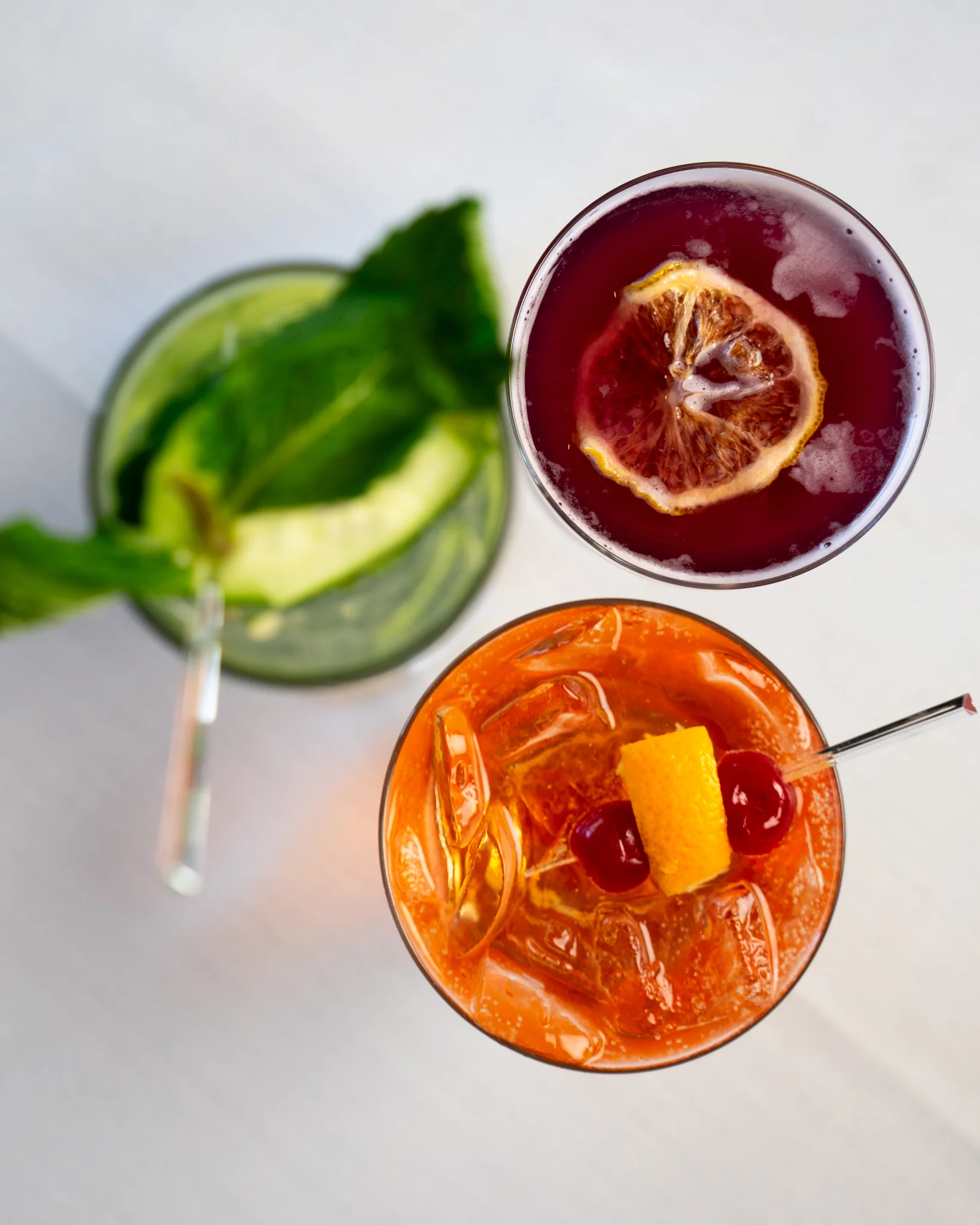 Three colorful cocktails with garnishes on a light background.