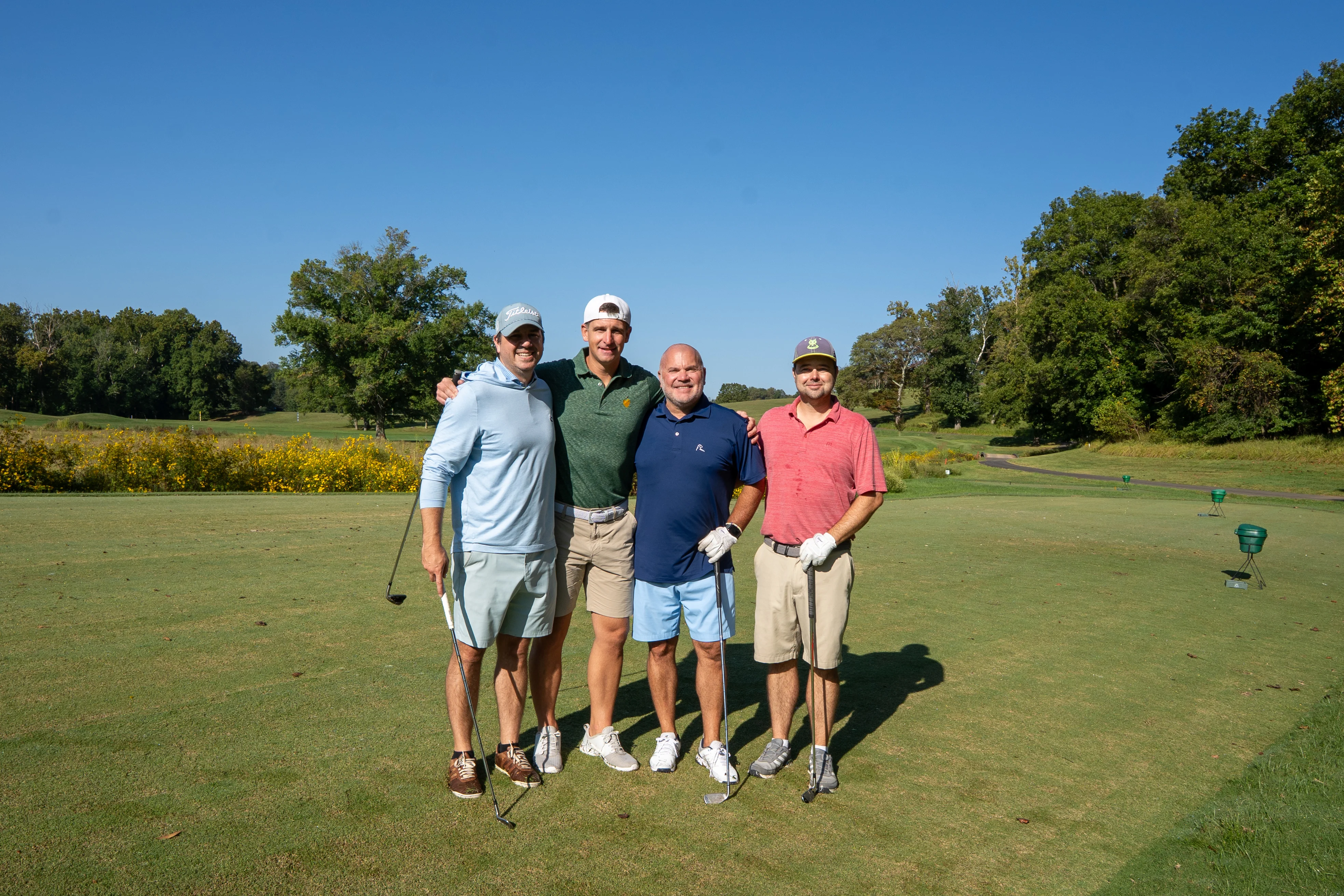 Four friends posing together on a golf course on a sunny day.
