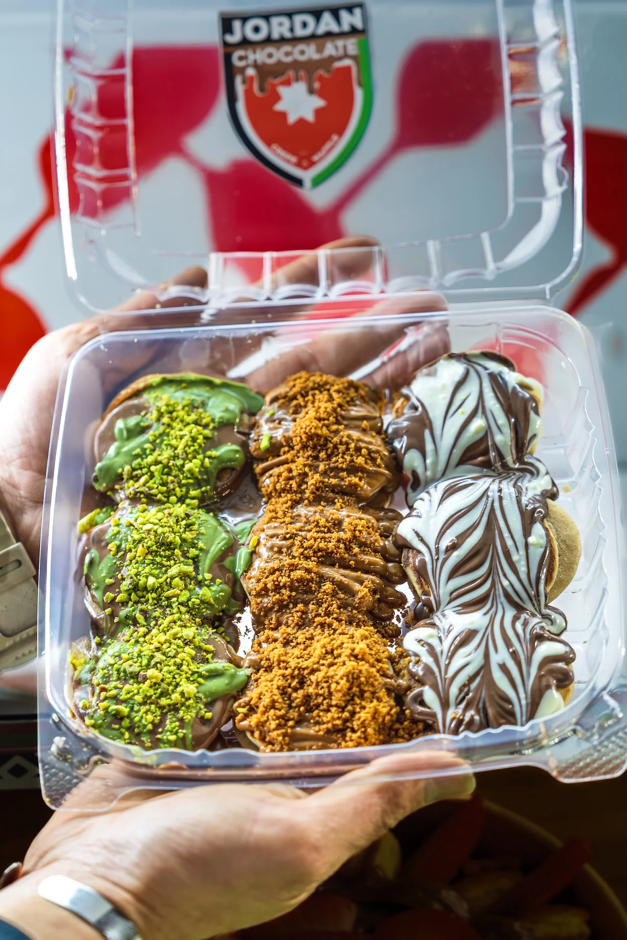 A plastic container filled with assorted chocolate treats, featuring different toppings like pistachios and a swirl design.