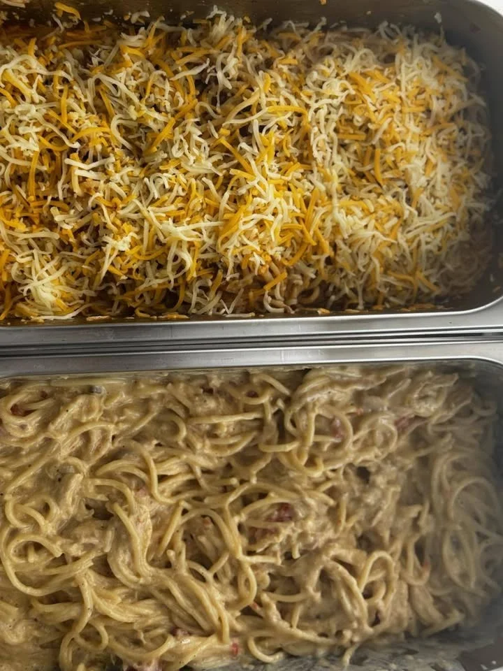 A tray featuring two different dishes: one with spaghetti and creamy sauce, the other topped with a blend of cheeses.