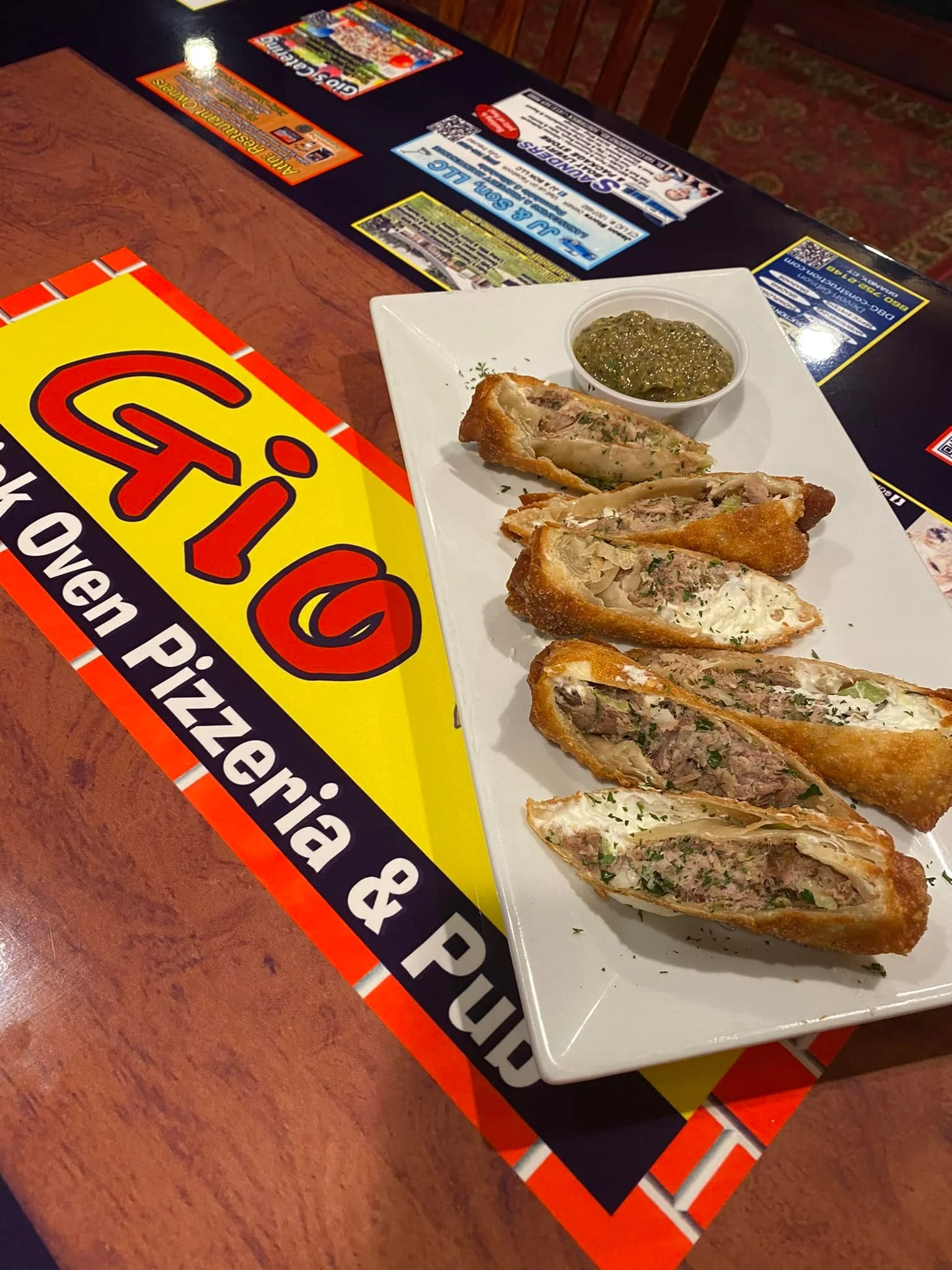 A plate of crispy fried rolls filled with meat, served with a small bowl of sauce on the side, positioned on a restaurant table.