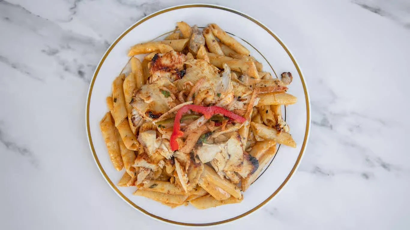 A plate of penne pasta topped with grilled chicken strips, garnished with colorful bell peppers and herbs.