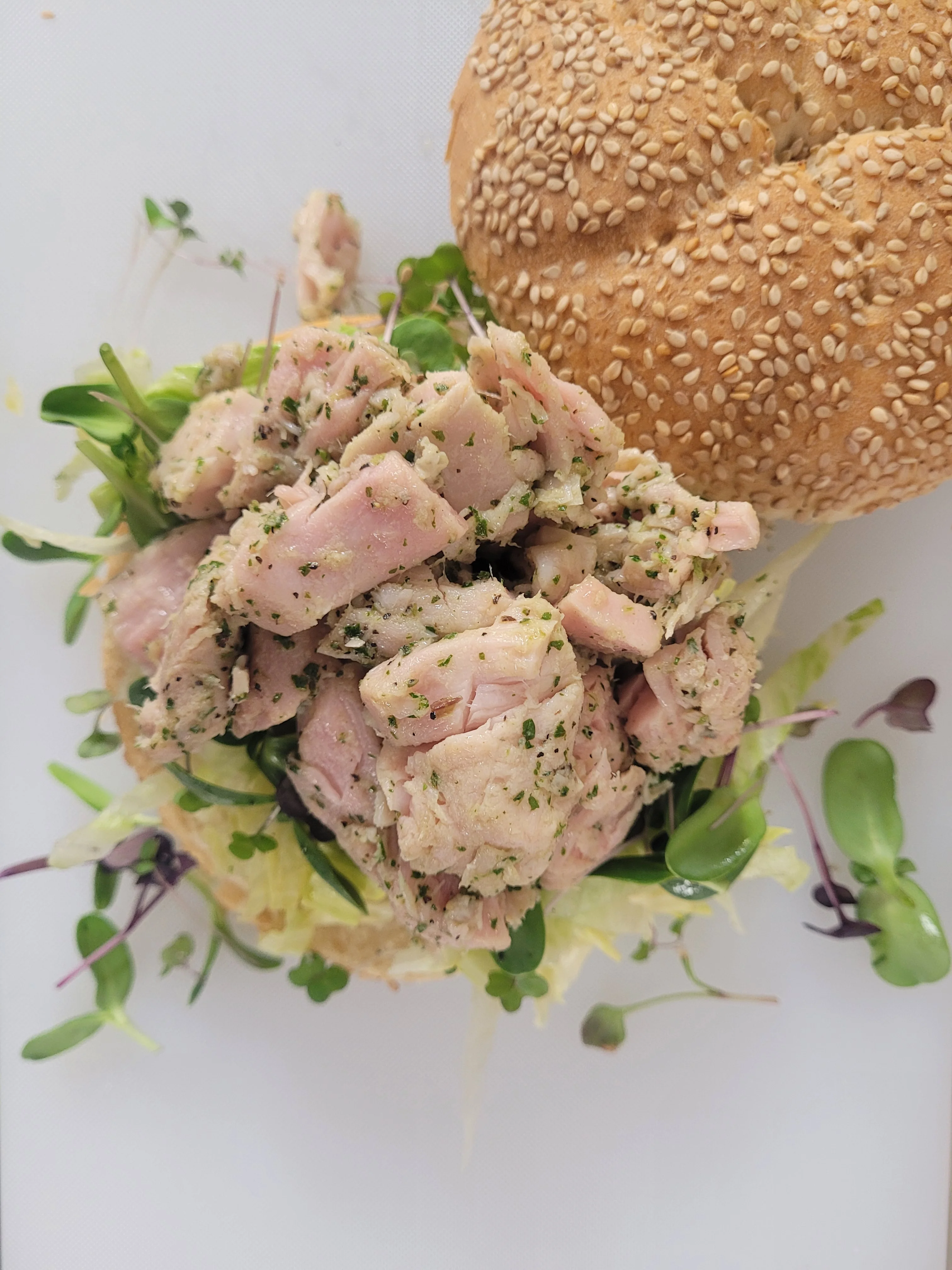 A lobster roll topped with a generous portion of lobster meat, lettuce, and served with a side of flavored oil.
