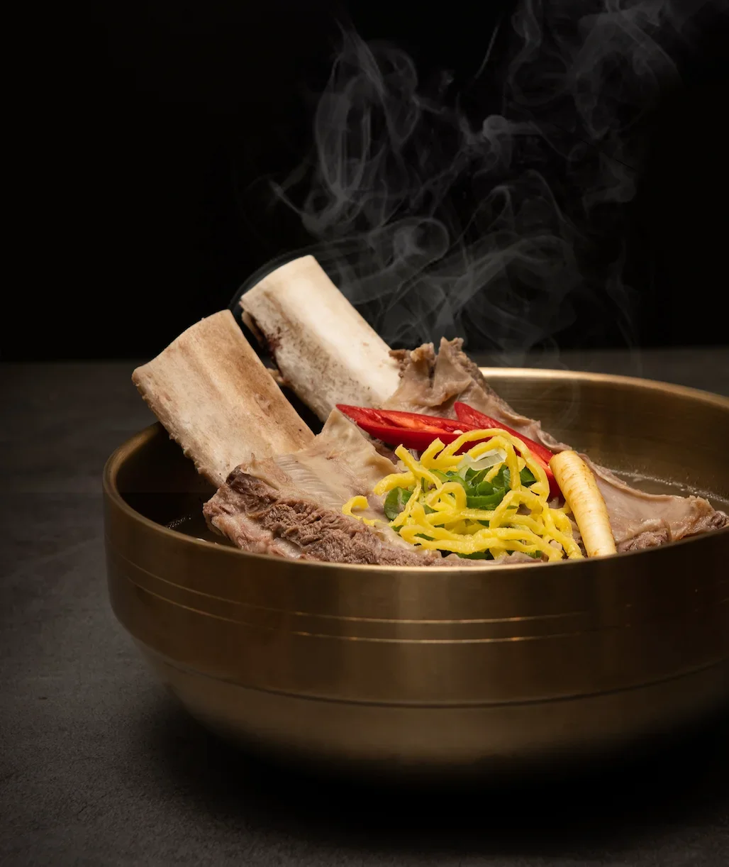A colorful platter of assorted Korean dishes, including sliced meat, various fresh greens, and spicy side dishes, accompanied by dipping sauces.