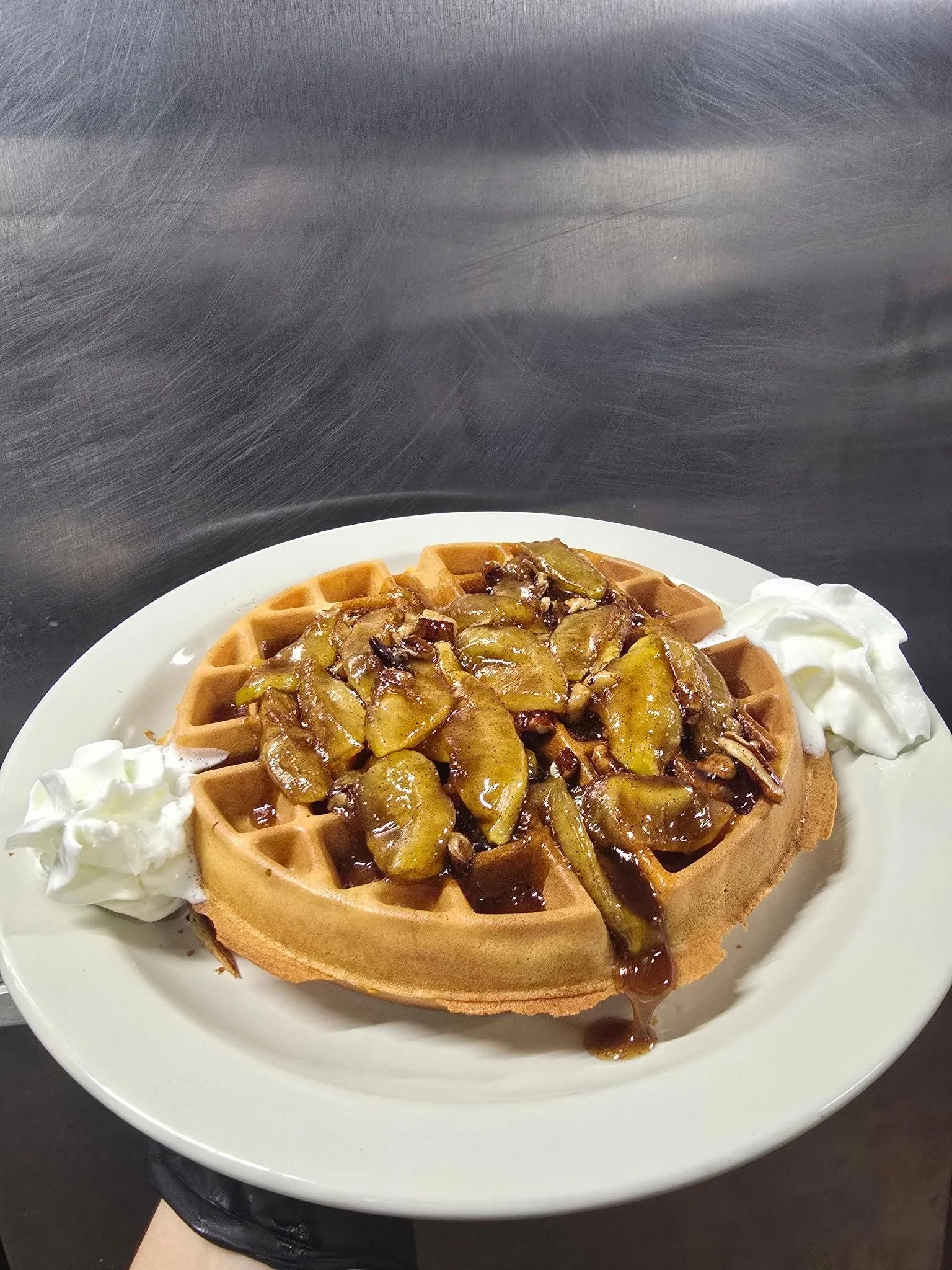 A plate of waffles topped with caramelized apple slices and a drizzle of syrup, accompanied by dollops of whipped cream.