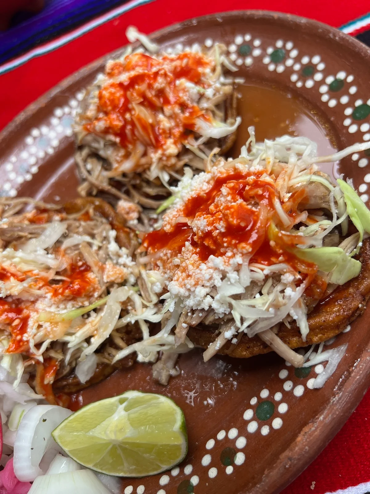 A decorative plate of tacos topped with shredded cabbage, cheese, and sauce, accompanied by lime and onions.