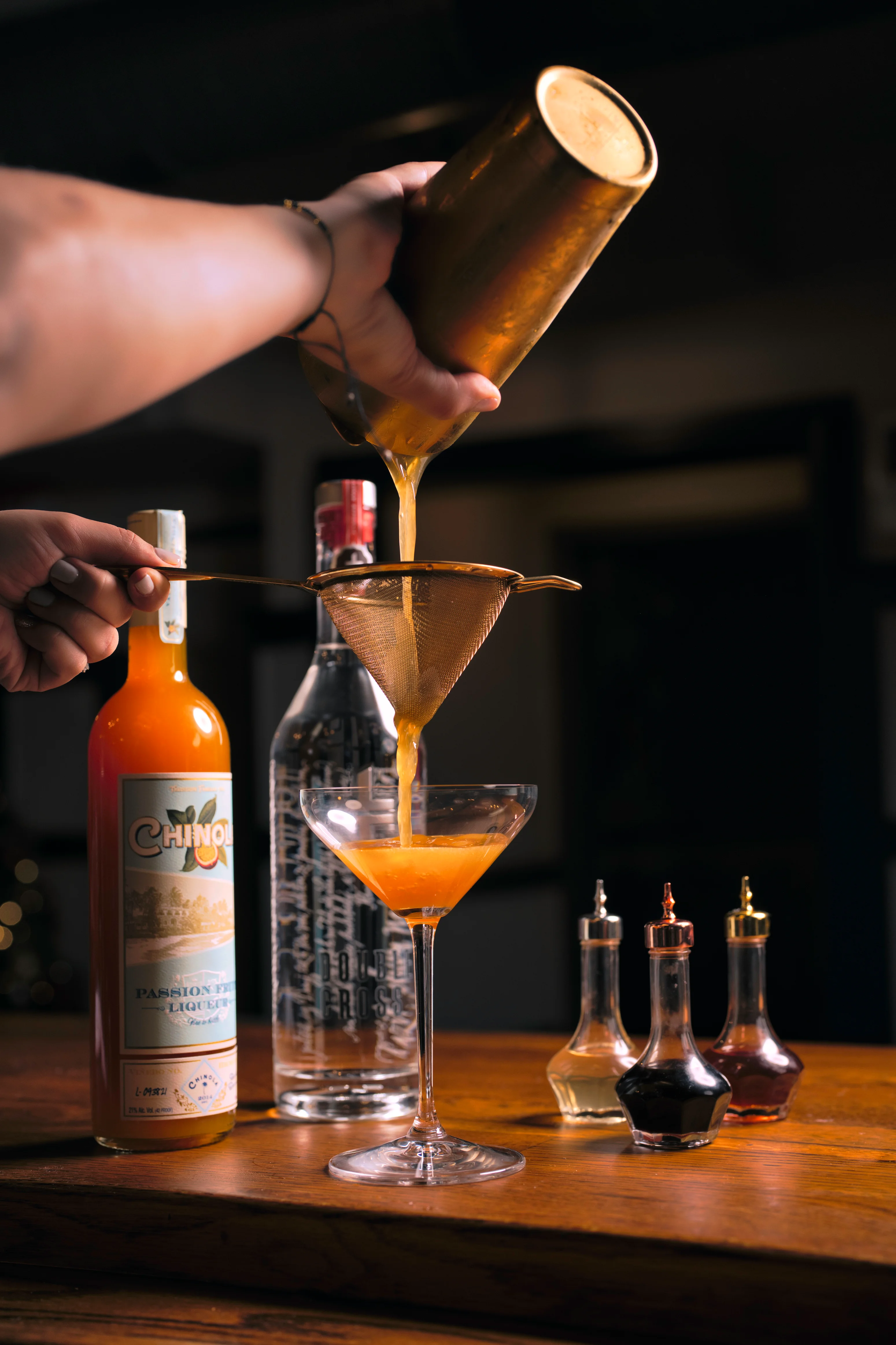 Bartender pouring a vibrant cocktail through a strainer