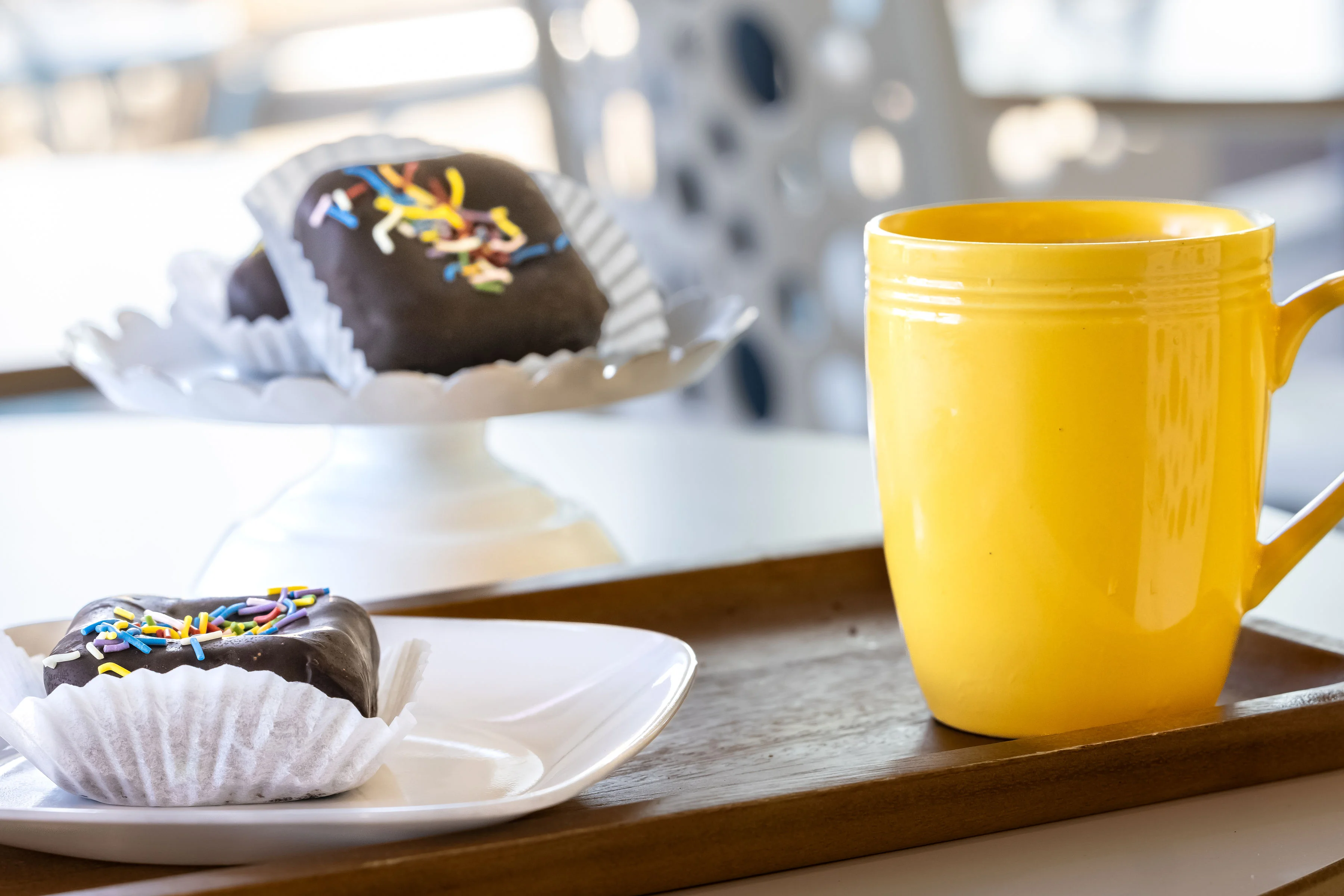 A delicious chocolate treat topped with colorful sprinkles, placed on a white dish with a yellow mug beside it.