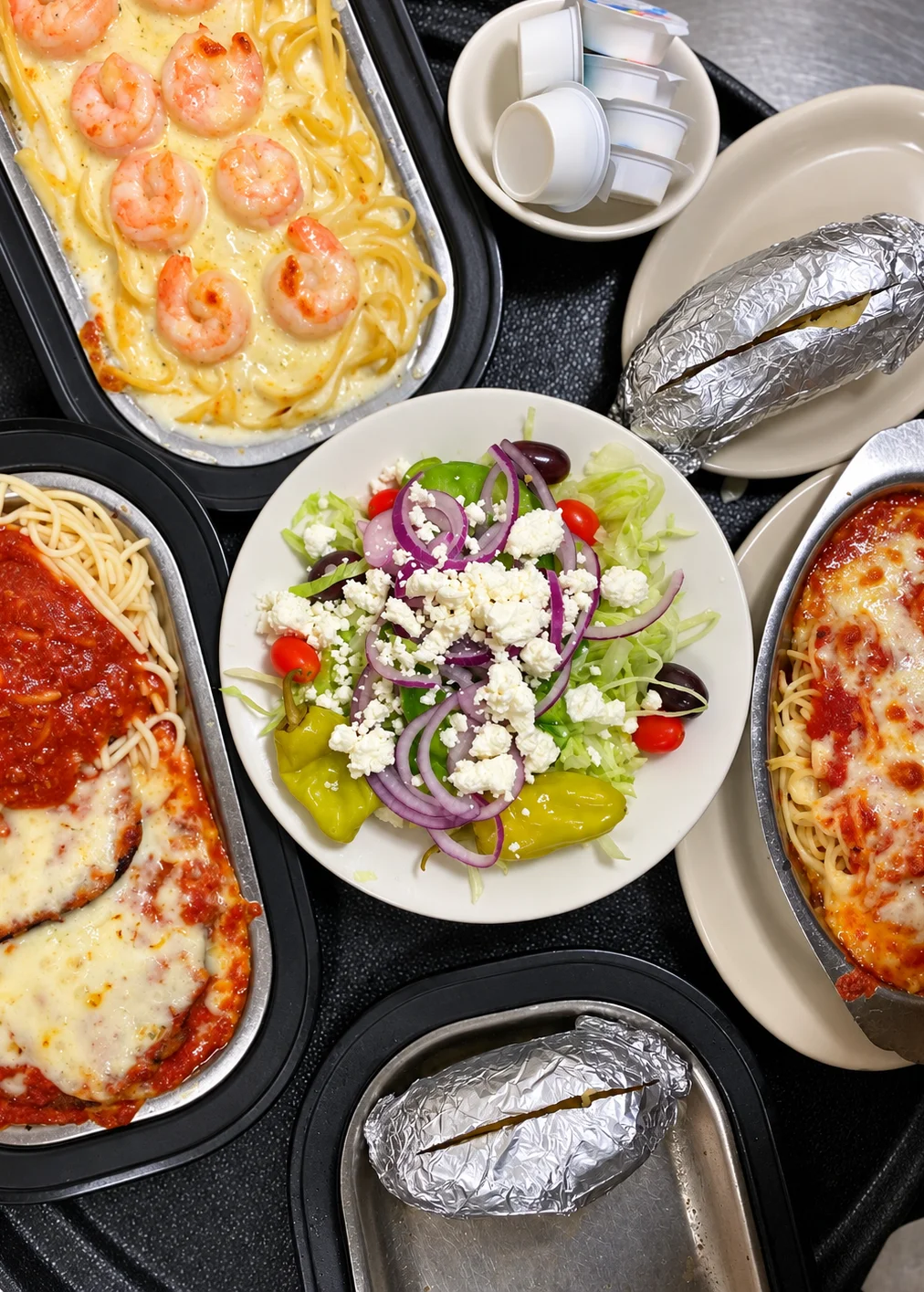 Italian-American takeout spread with shrimp Alfredo, chicken parmesan, Greek salad, and baked potatoes