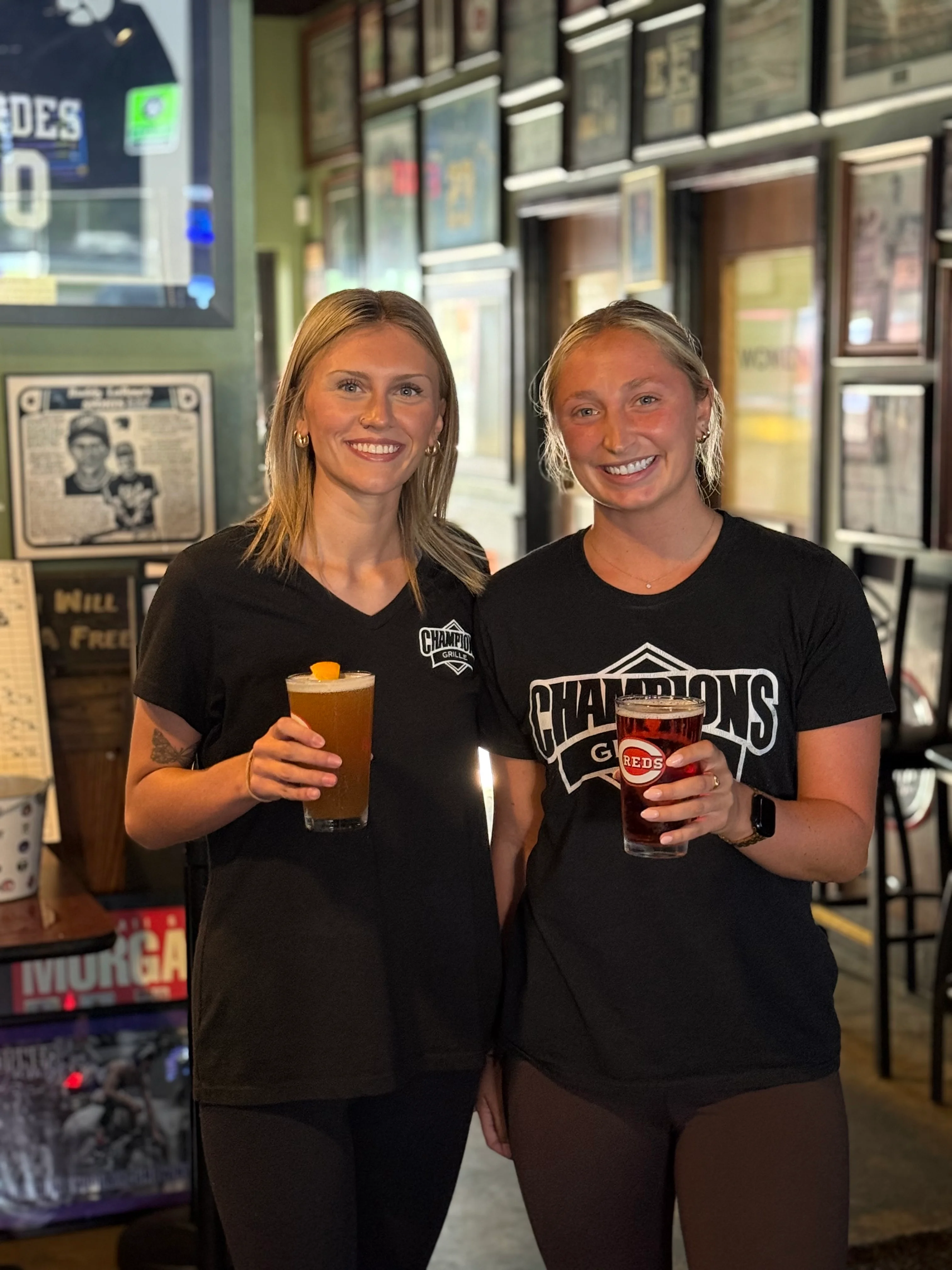 Two bartenders holding drinks in a lively restaurant setting