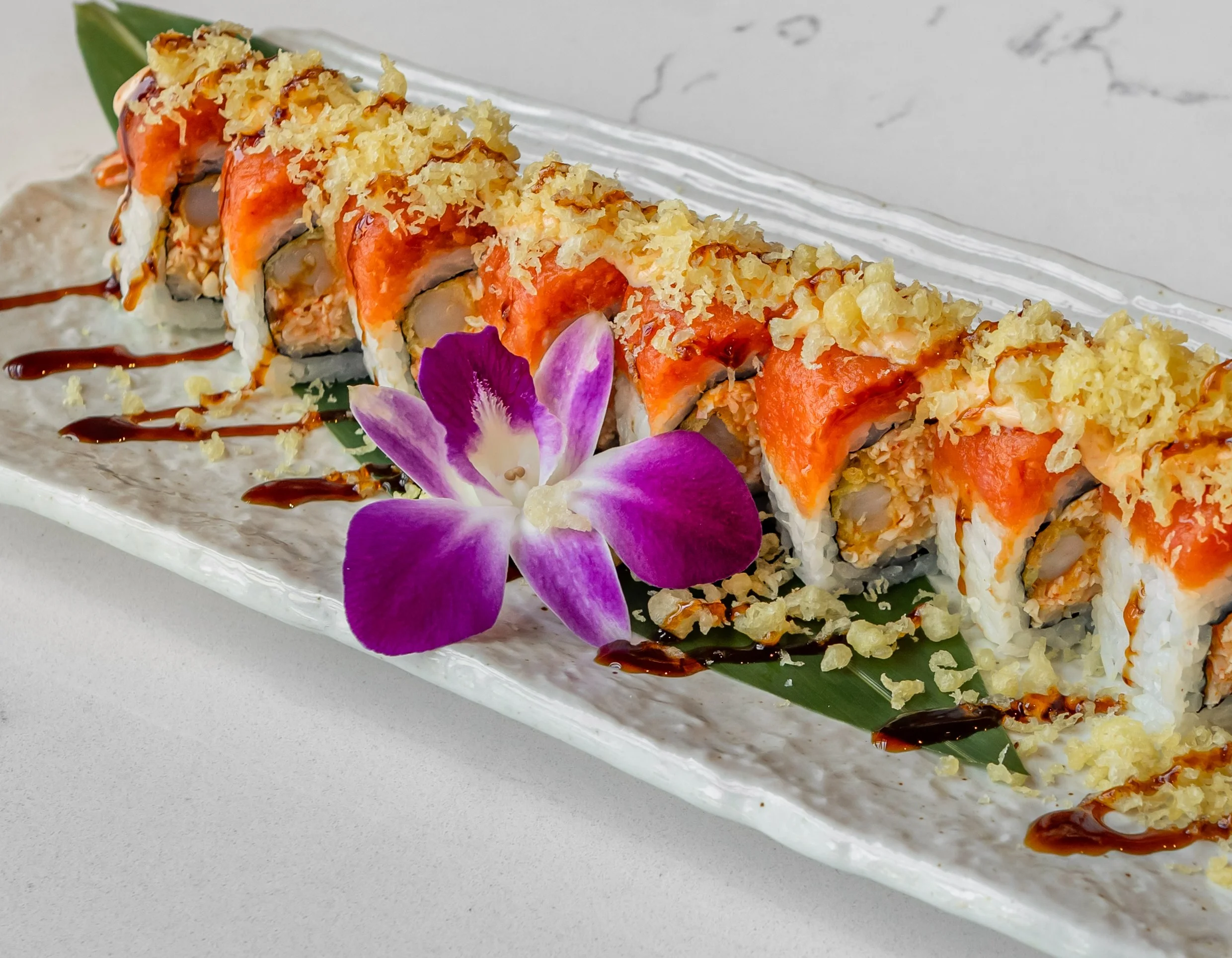 Japanese sushi roll topped with crispy tempura flakes and garnished with a flower