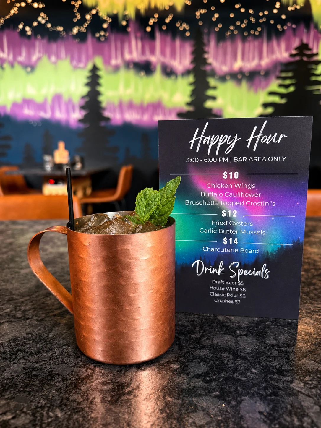 A copper mug filled with a drink garnished with mint, placed next to a menu featuring happy hour specials and drink options.