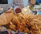 A serving of fried chicken, French fries, a bread roll, and dipping sauces presented on a tray.
