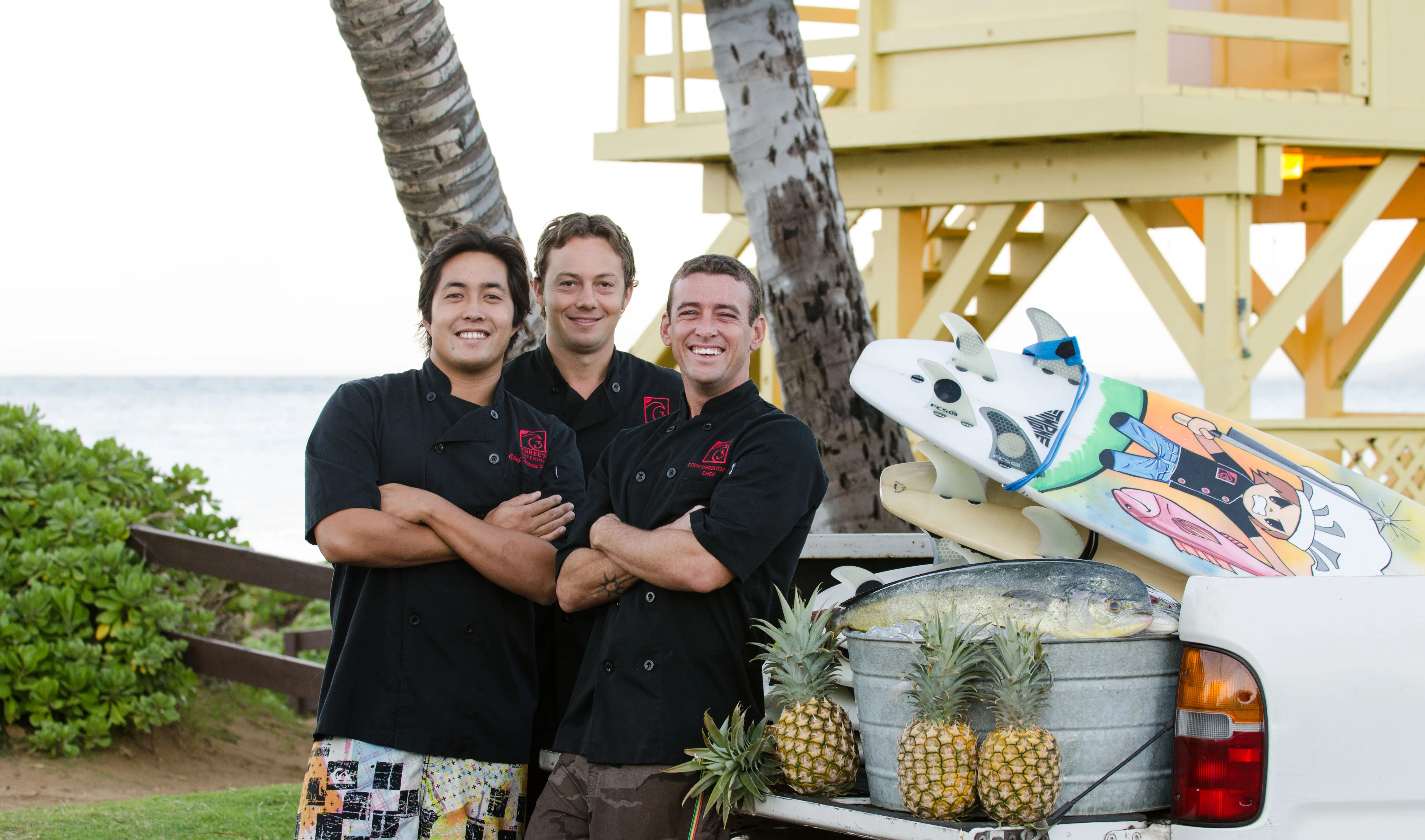 Chefs posing with surfboards and pineapples by the beach