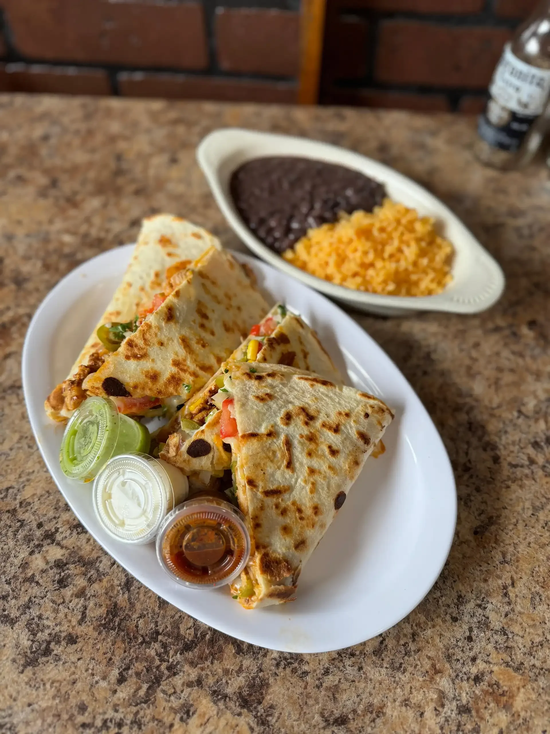 A delicious plate of freshly grilled quesadillas, served with sour cream, salsa, guacamole, and a side of rice and black beans.