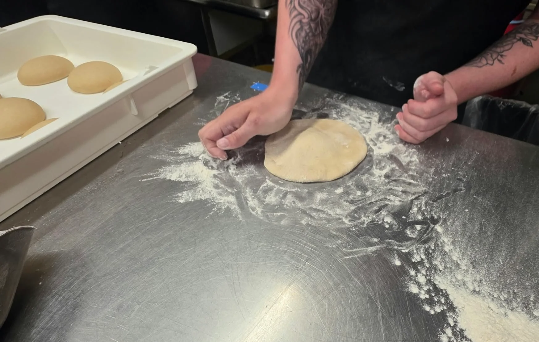 Restaurant cook shaping fresh pizza dough on a floured stainless steel worktable
