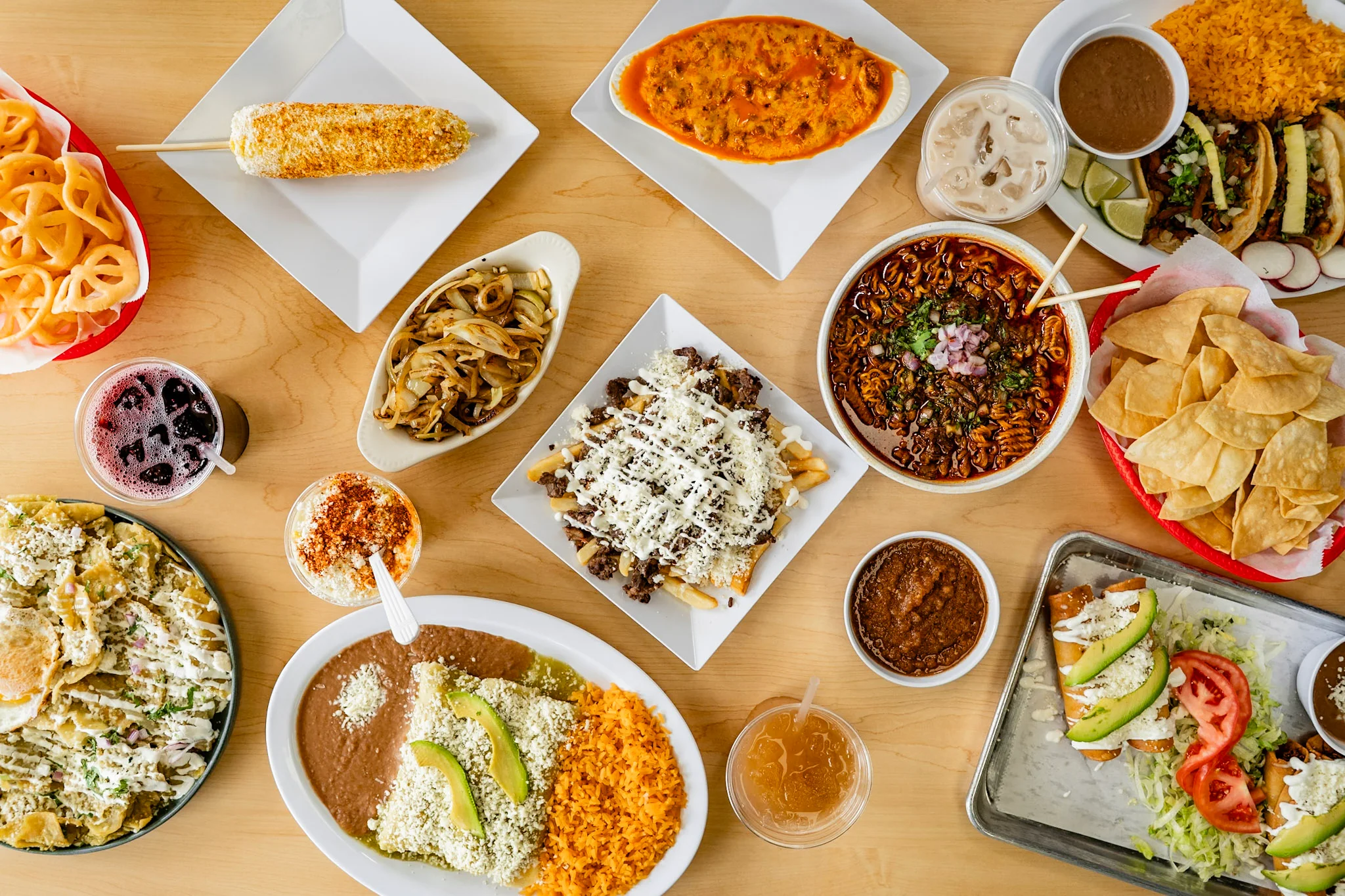 Colorful Mexican feast featuring tacos, elote, and nachos on a wooden table