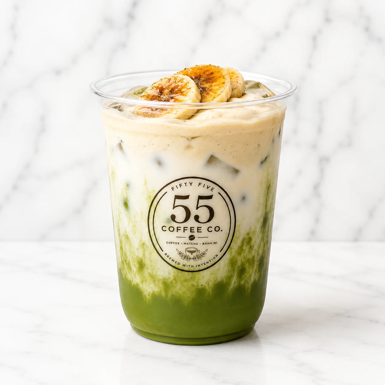 A layered green tea beverage topped with banana slices, served in a clear cup showcasing vibrant colors.