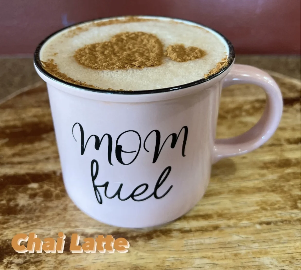 A pink mug labeled 'MOM fuel' filled with a frothy chai latte and sprinkled with cinnamon.