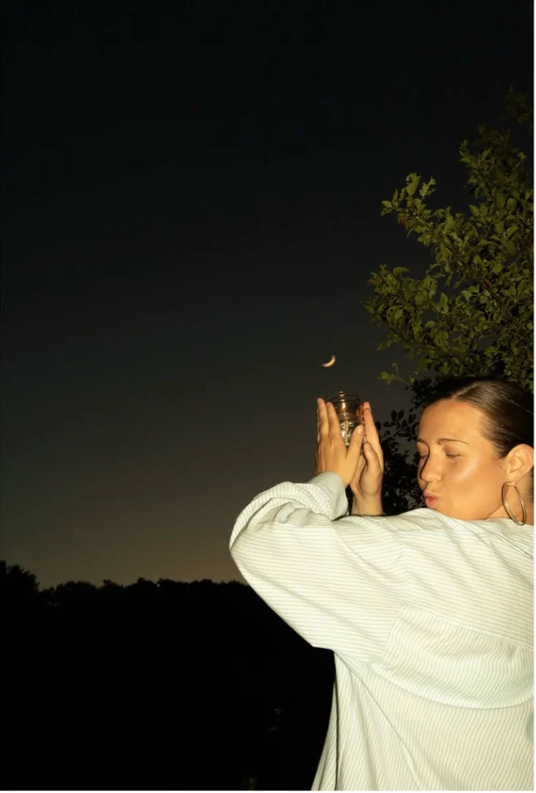 Person holding a jar under a crescent moon at dusk
