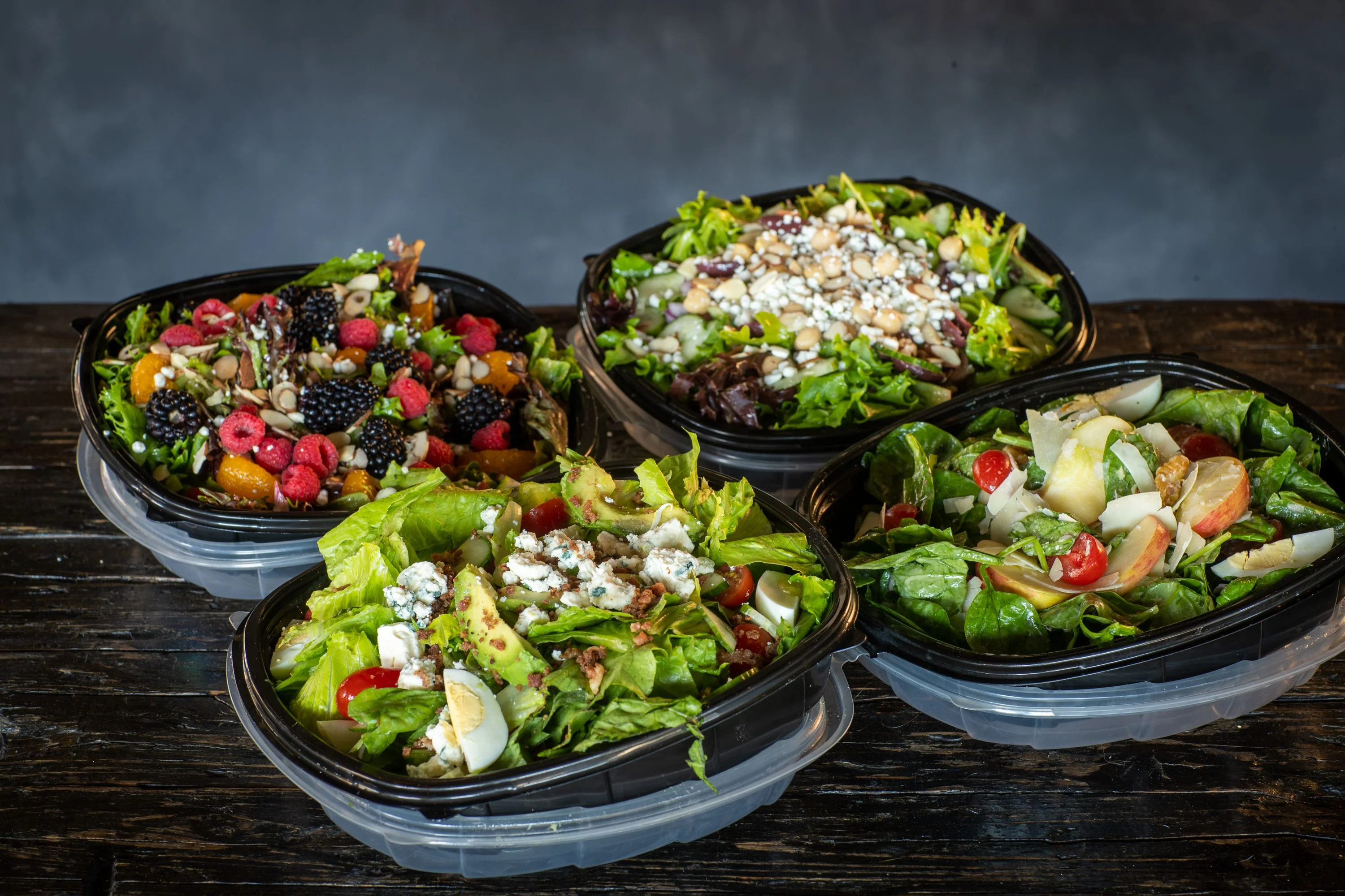 Assorted gourmet salads in black containers, showcasing fresh ingredients and vibrant colors