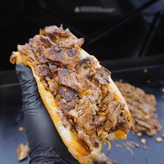 A handheld sandwich overflowing with grilled meat and cheese, held in gloved hands, showcasing its delectable filling.