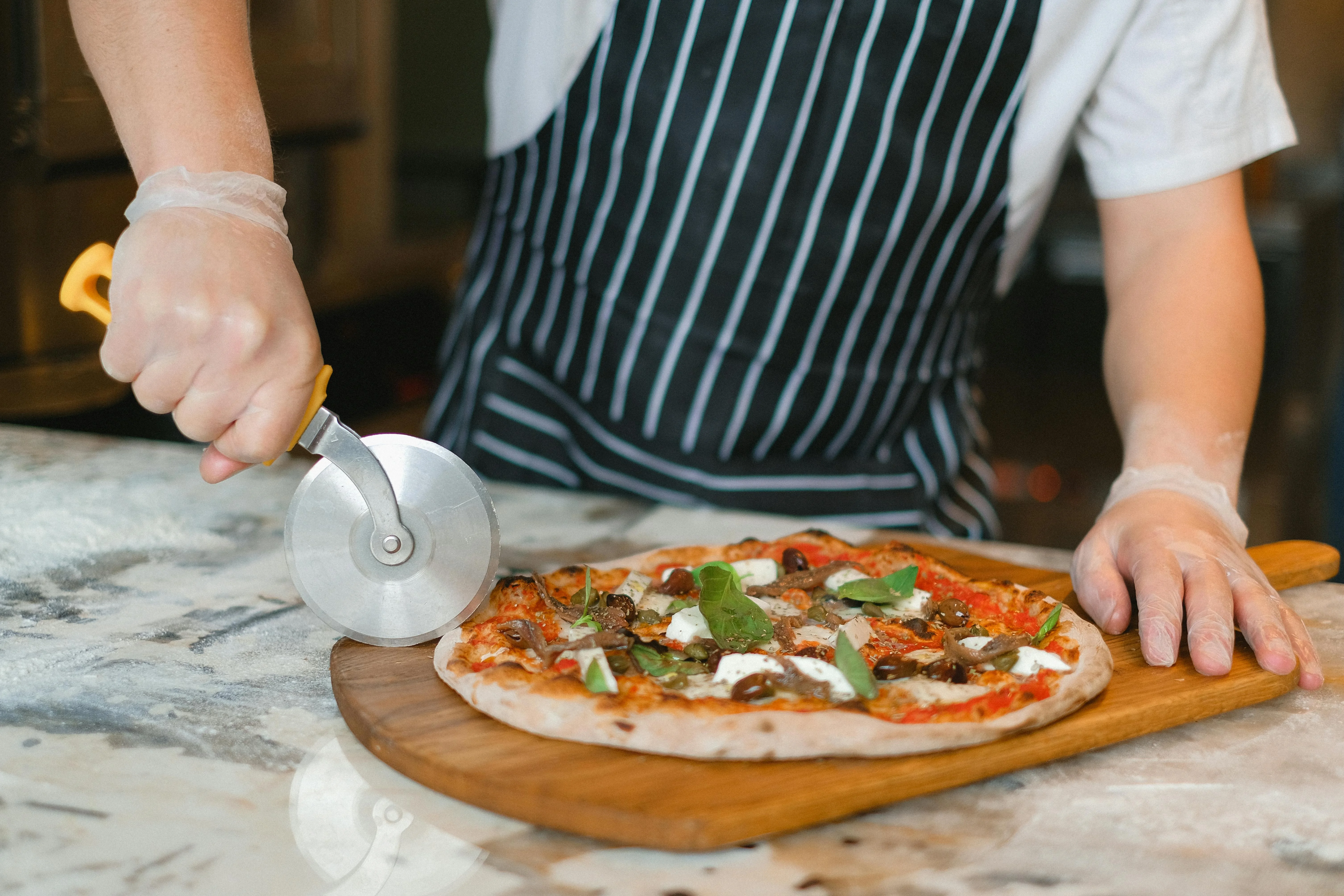 Chef slicing a Margherita pizza with a pizza cutter