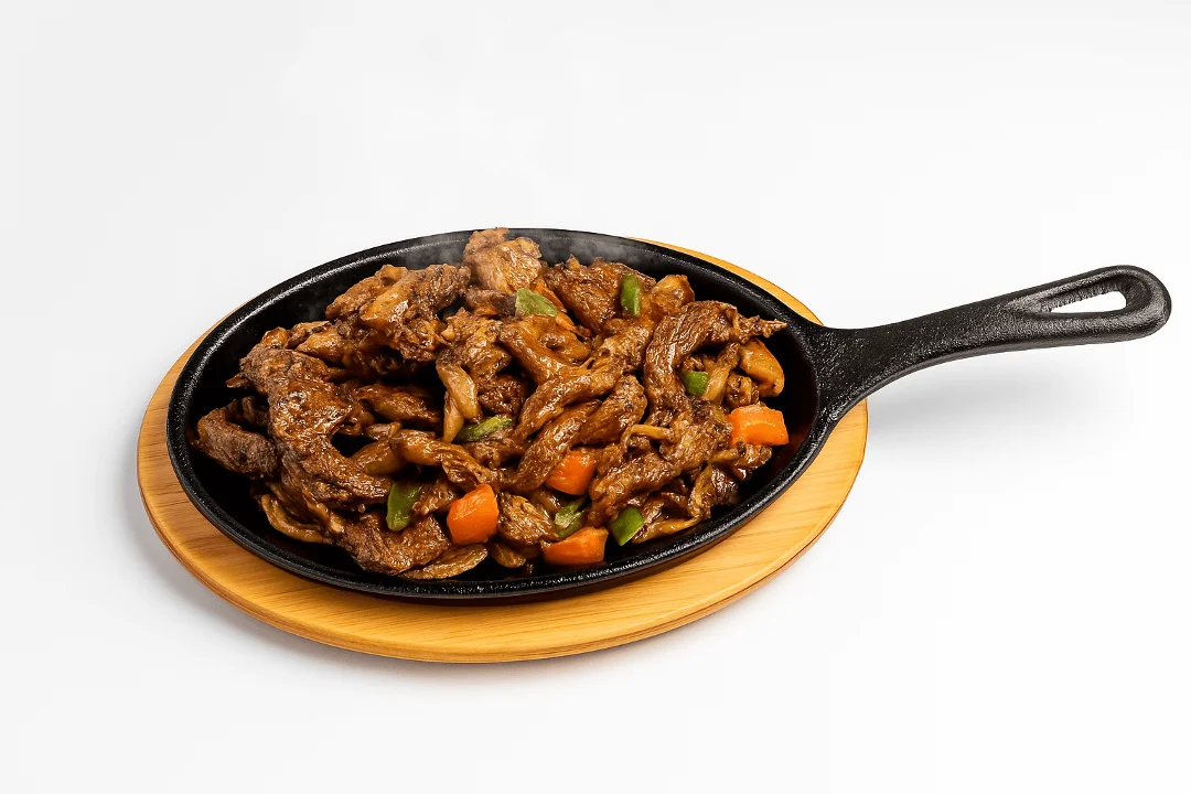 Sizzling beef with vegetables served on a hot cast iron skillet, showcasing tender strips of meat and colorful veggies.