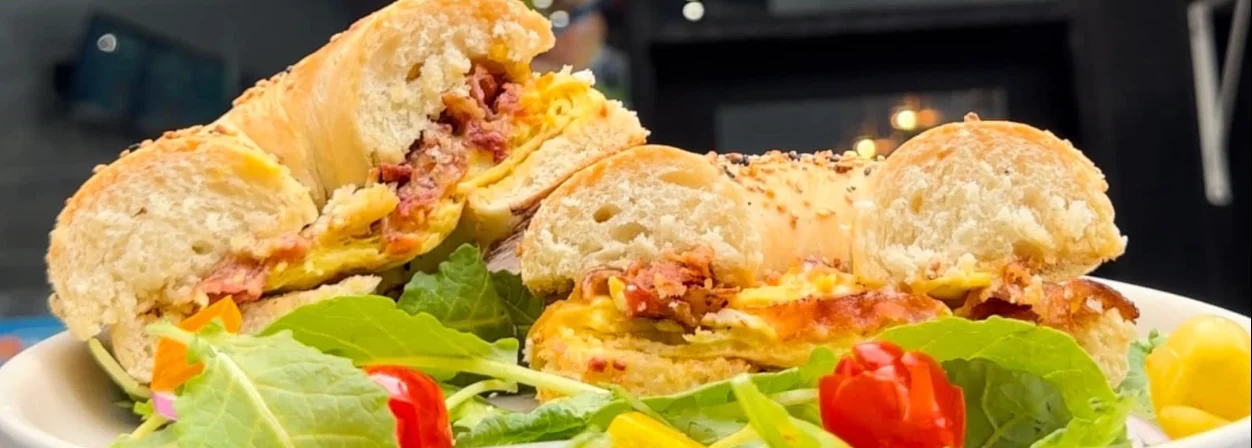 A close-up of a sandwich cut in half, showcasing layers of meat and cheese, served on a plate with a side of fresh salad and colorful vegetables.