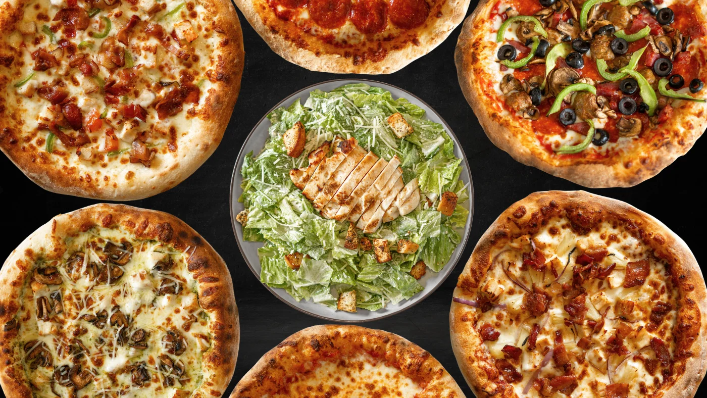 Assorted pizzas including pepperoni and a Caesar salad centerpiece