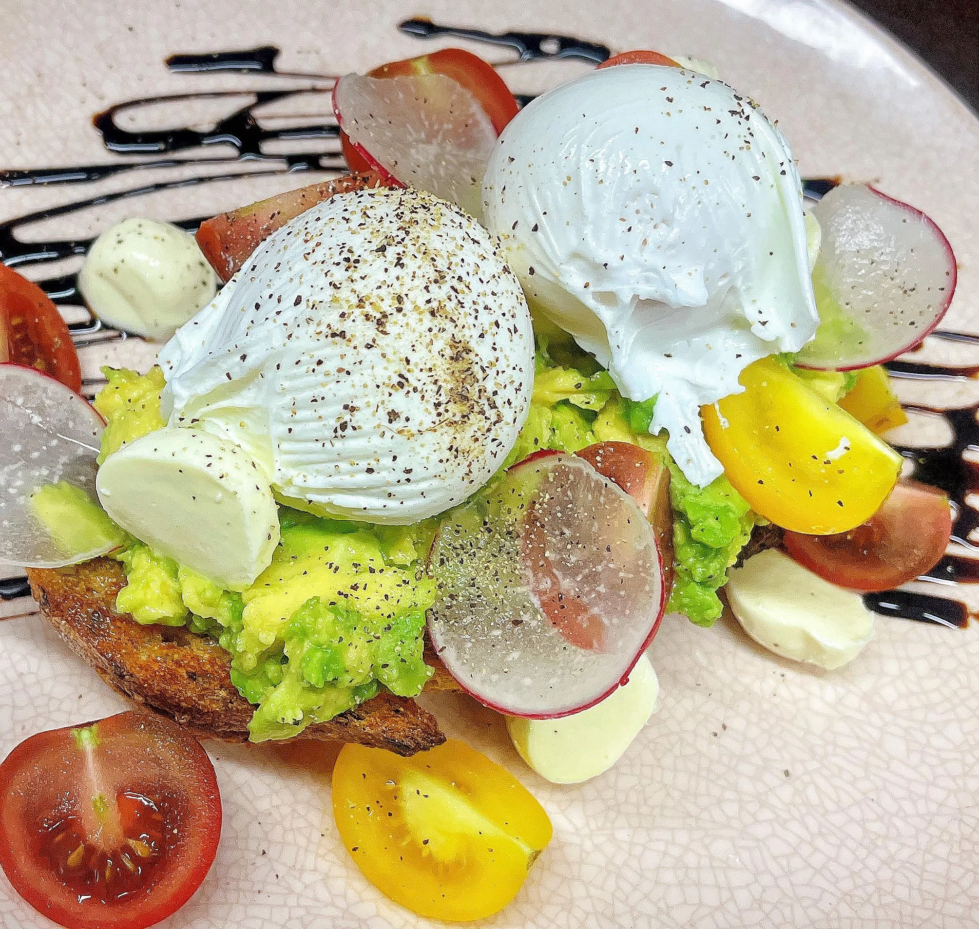 A vibrant plate of avocado toast topped with poached eggs, cherry tomatoes, and radishes, creating a colorful and fresh meal.