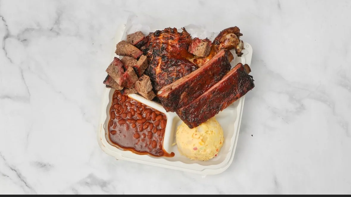 A delicious platter featuring grilled meat, including ribs and beef, accompanied by baked beans and a scoop of potato salad.