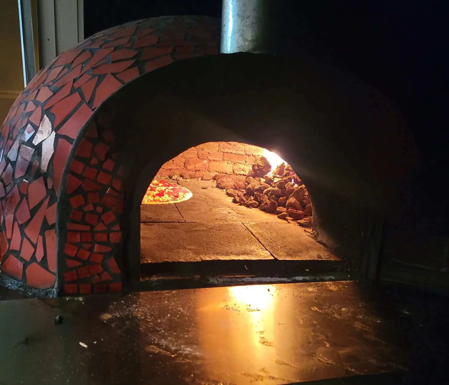 A vibrant red wood-fired oven nestled among trees, illuminated by soft string lights in a cozy outdoor setting.