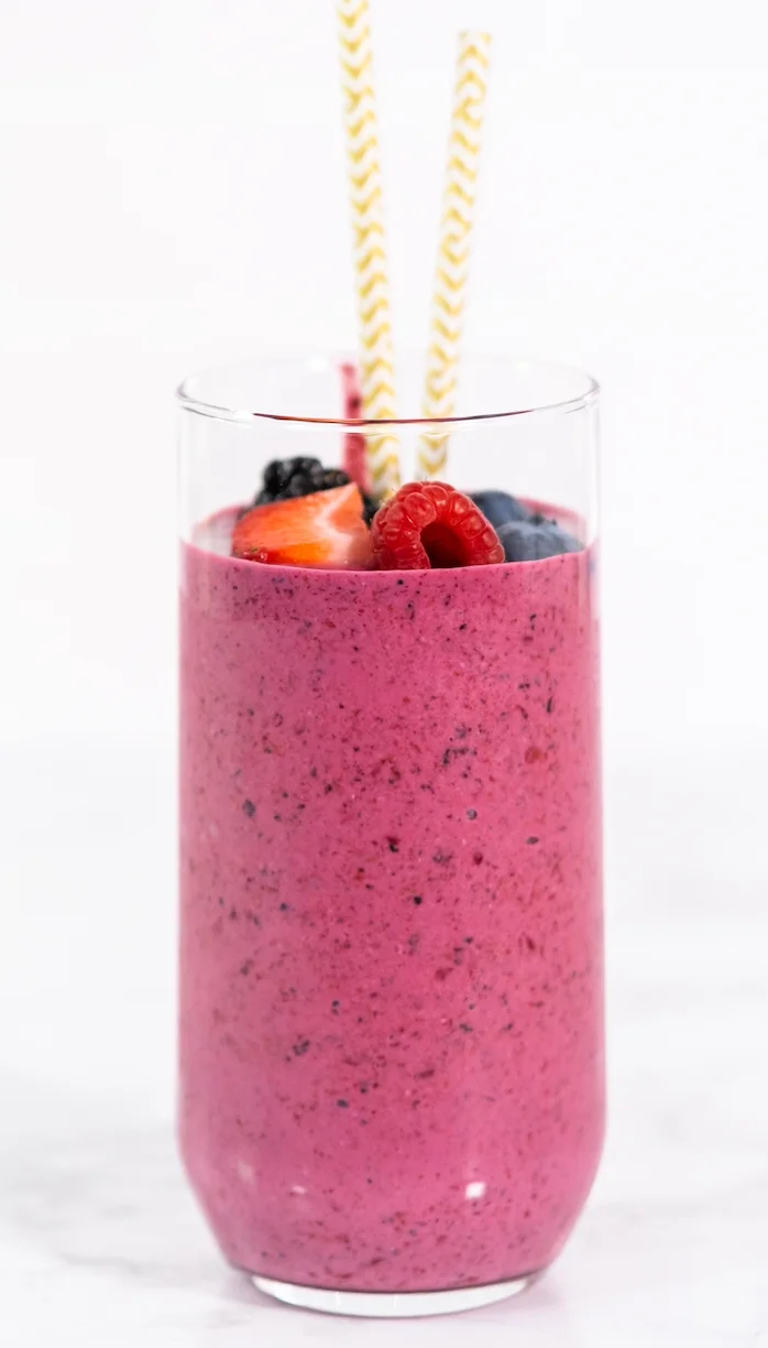 A vibrant smoothie made with various berries, topped with fresh fruit and served with striped straws.