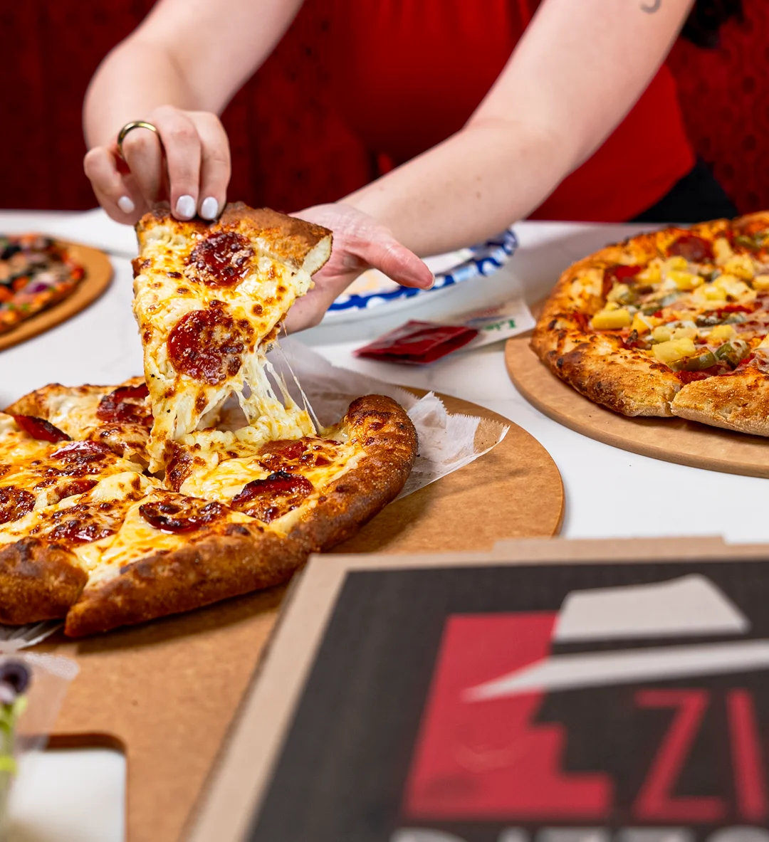 A hand reaching for a slice of pepperoni pizza with melted cheese.