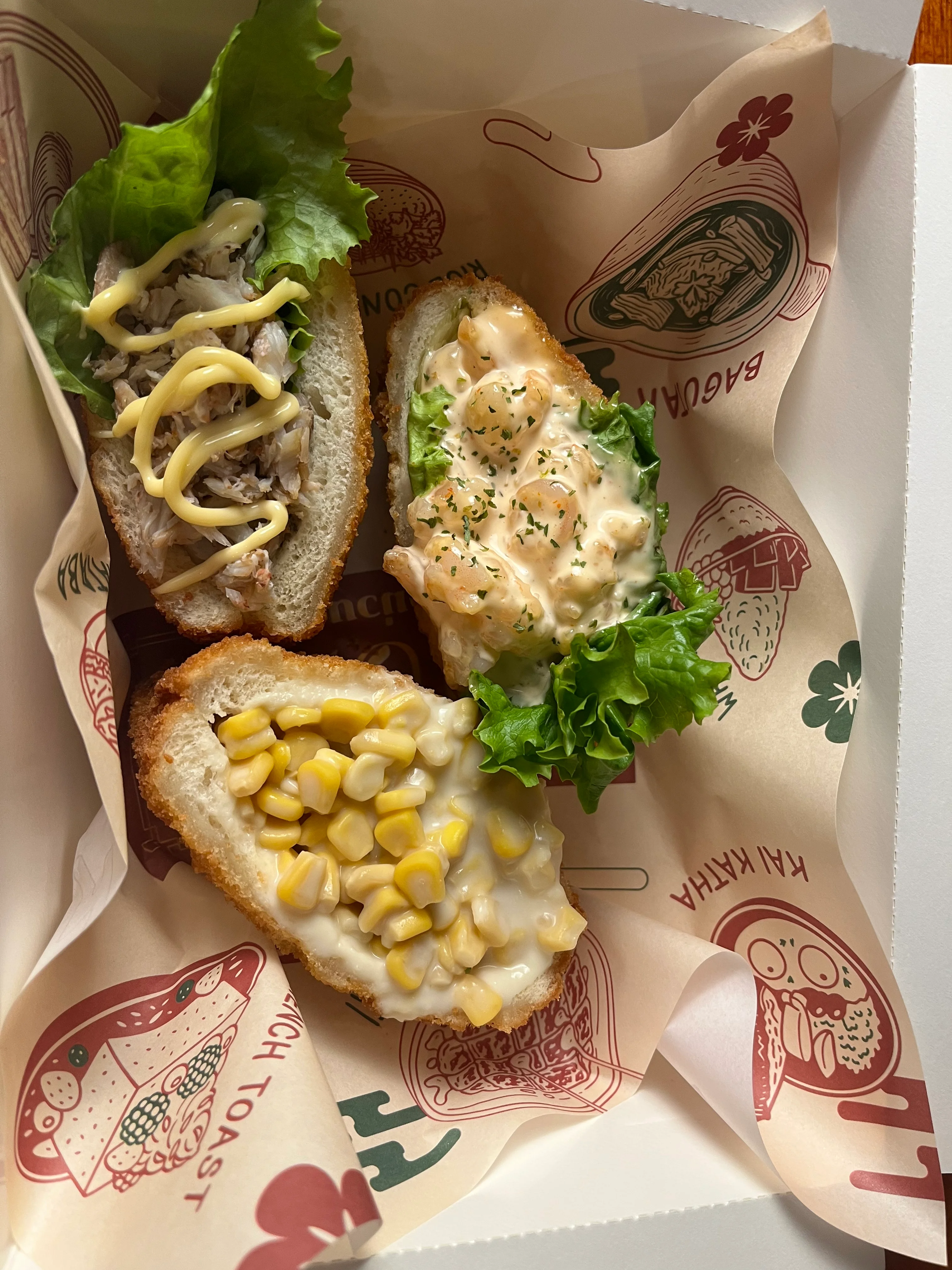 Three different sandwiches in a box, each topped with various ingredients including lettuce, mayonnaise, and corn.