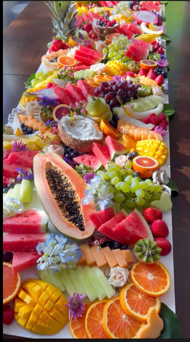 A vibrant fruit platter showcasing a variety of fresh fruits including watermelon, mango, berries, and citrus, beautifully arranged with flowers.
